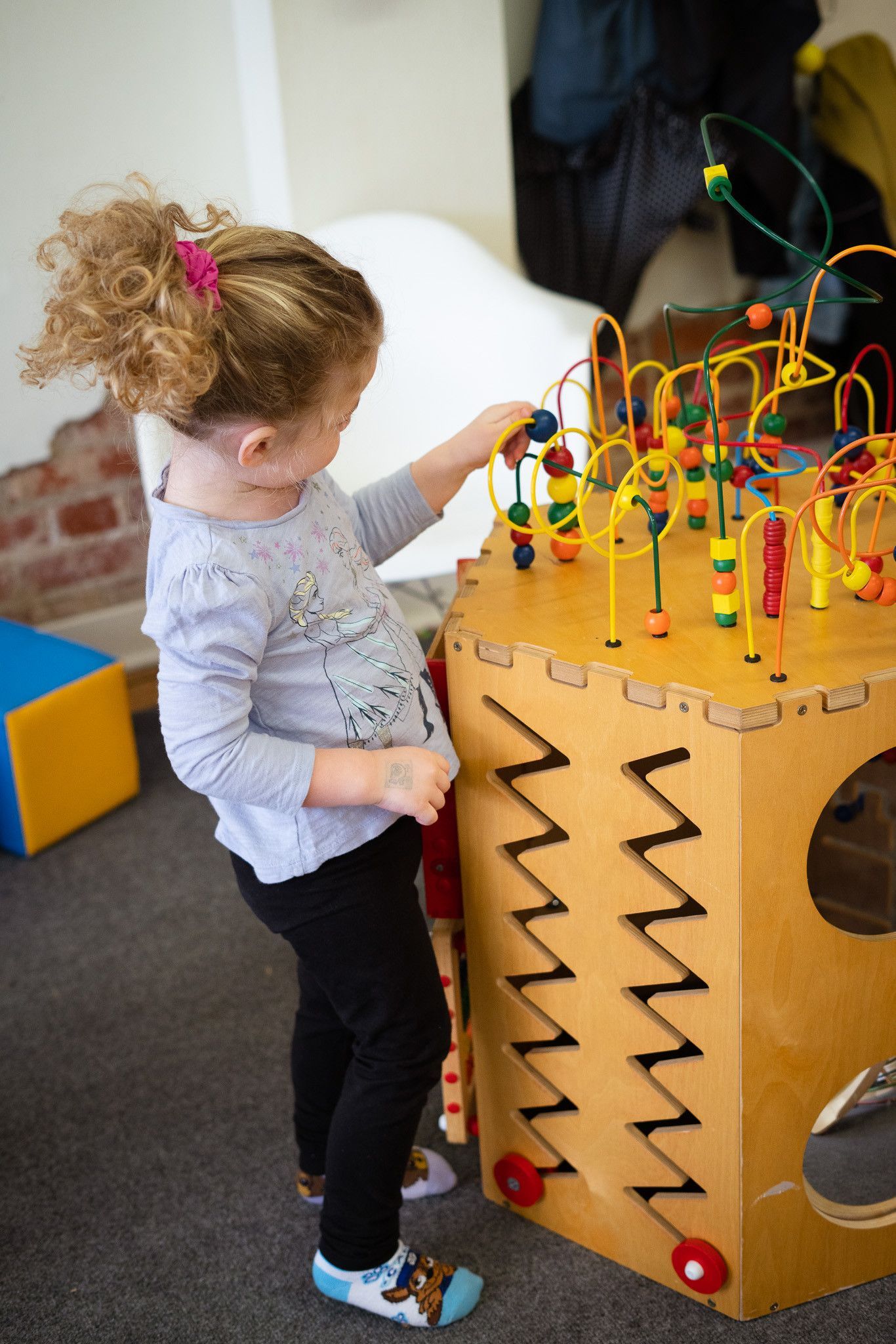 A little girl is playing with a wooden toy in a room.
