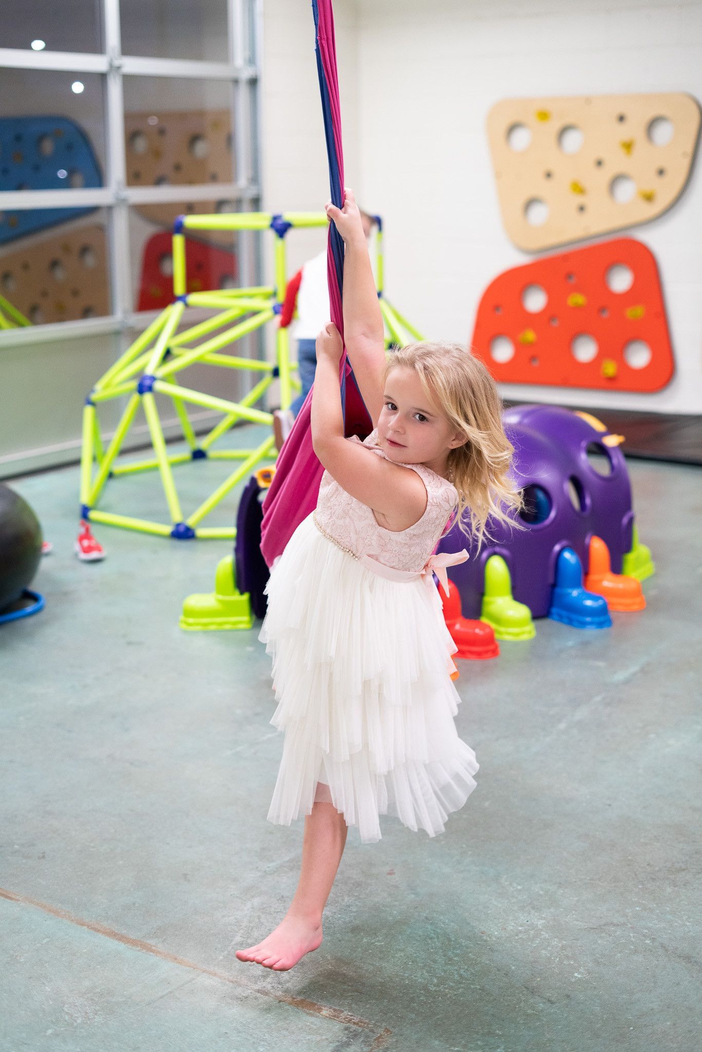 A little girl in a white dress is playing on a swing in a playground.