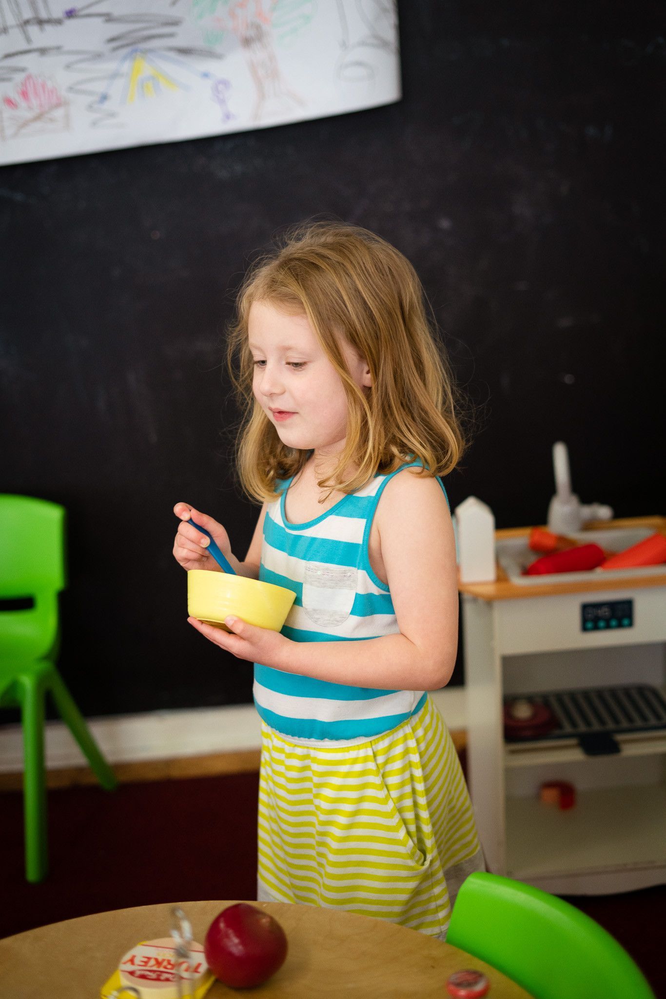 A little girl is standing at a table holding a bowl of cereal.