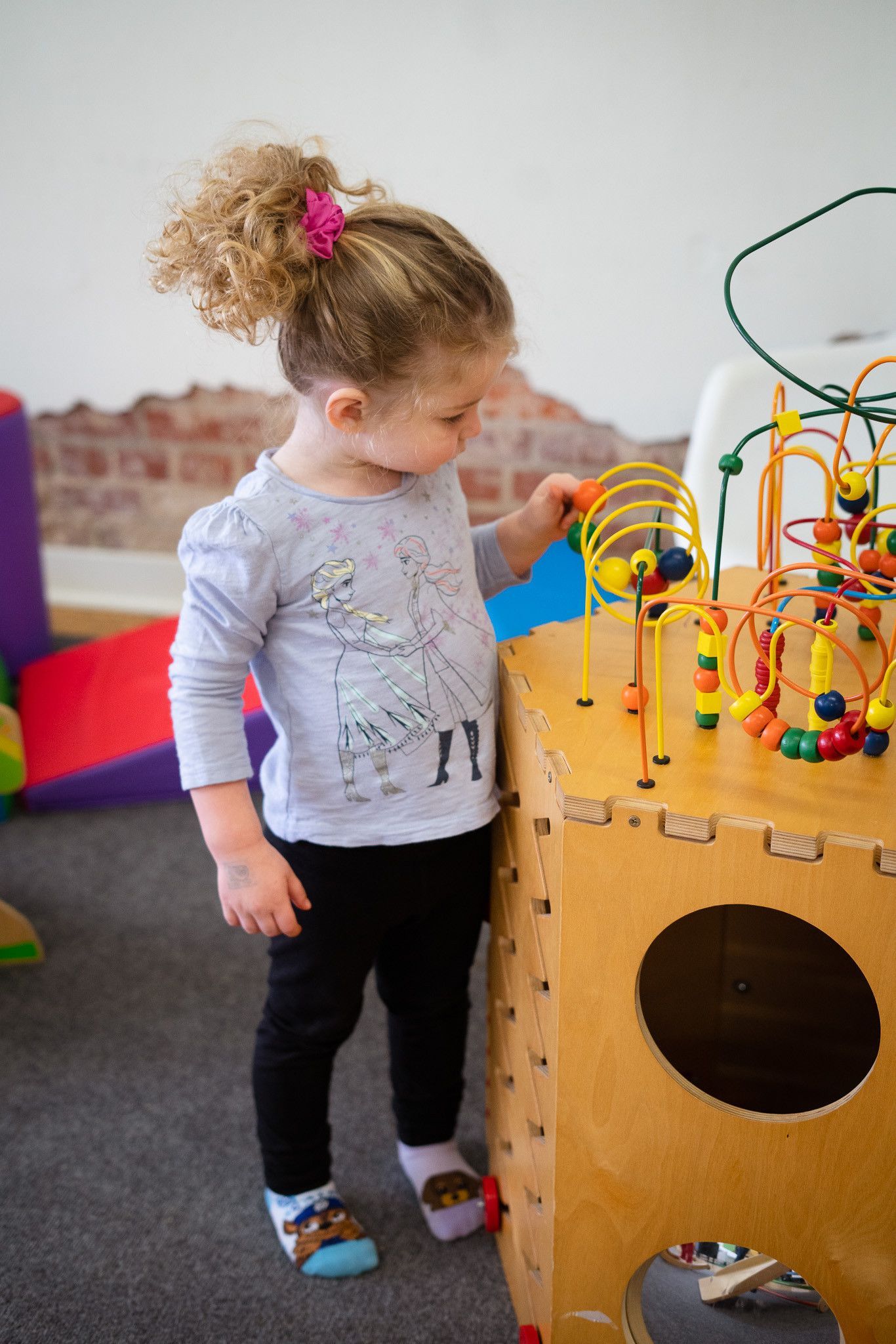 A little girl is playing with a wooden toy in a room.
