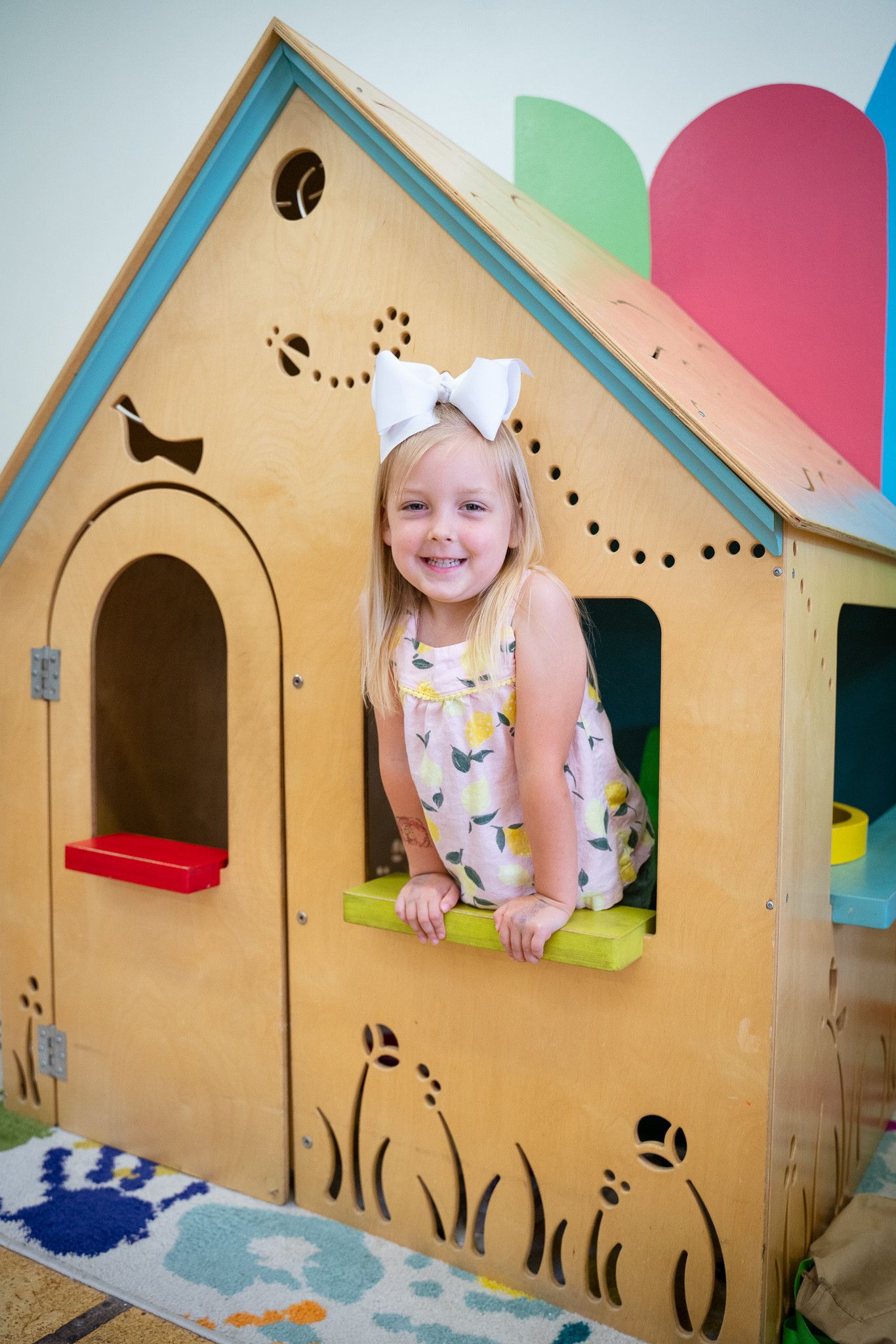 A little girl is sitting in a wooden playhouse.