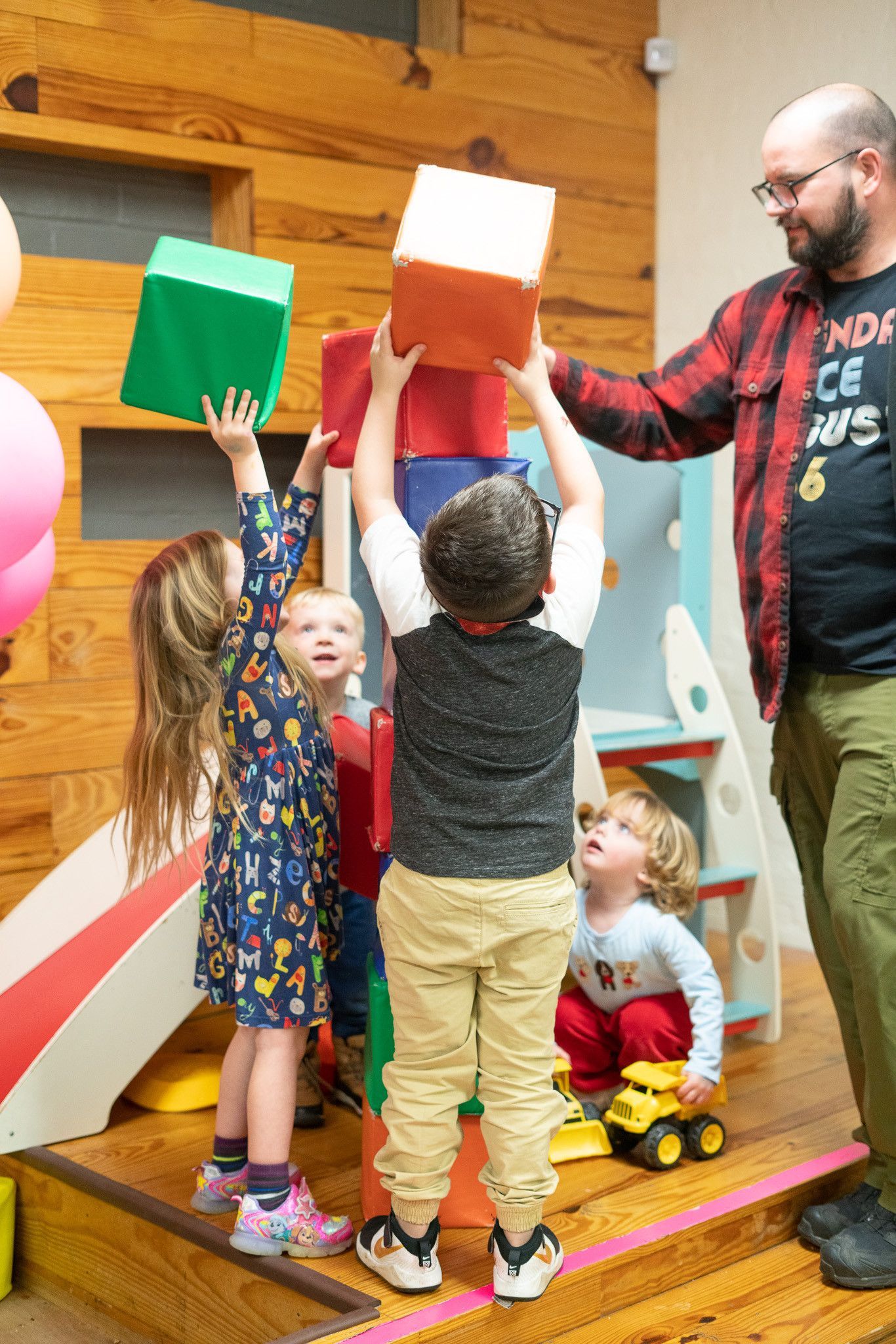 A man is standing next to a group of children playing with blocks.