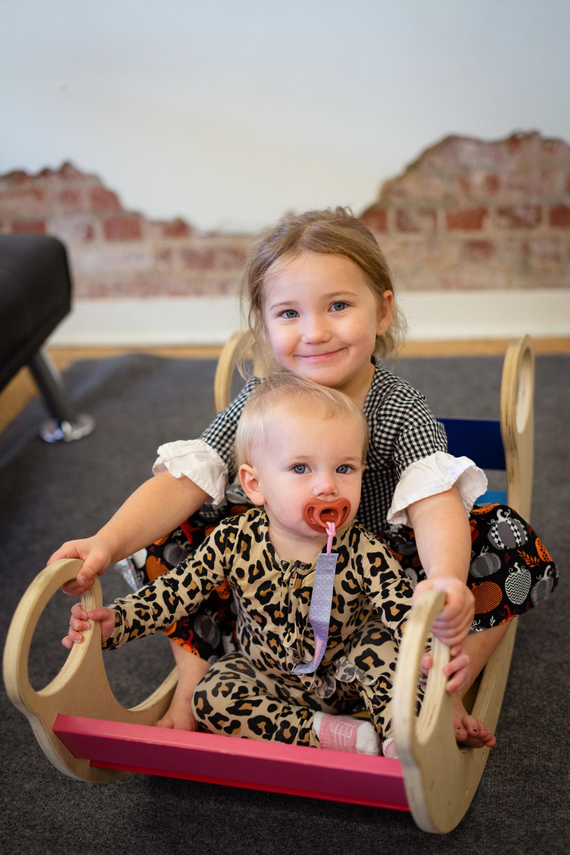 Two little girls are sitting on a wooden rocking chair.