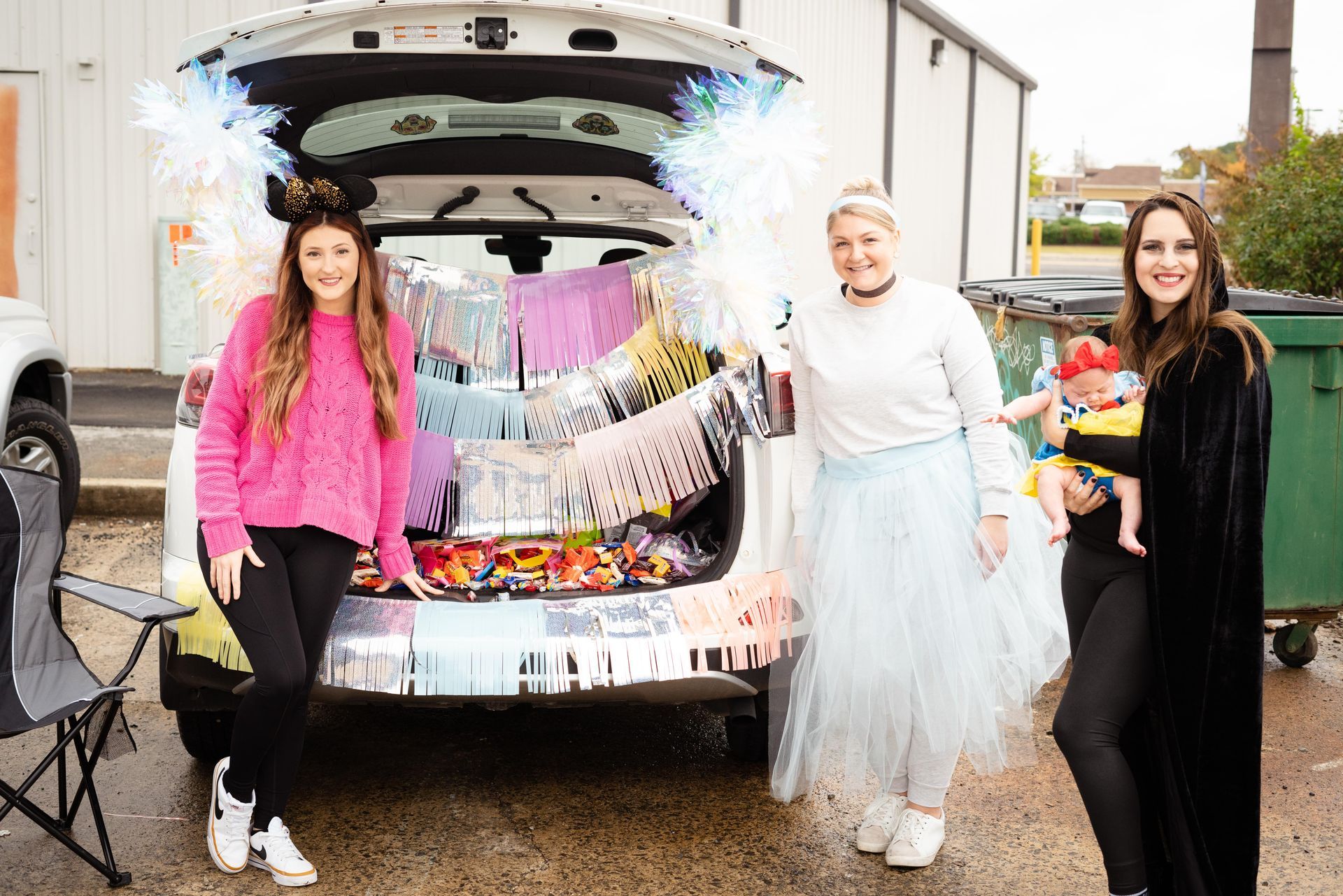 Three women are standing in front of a decorated trunk of a car.