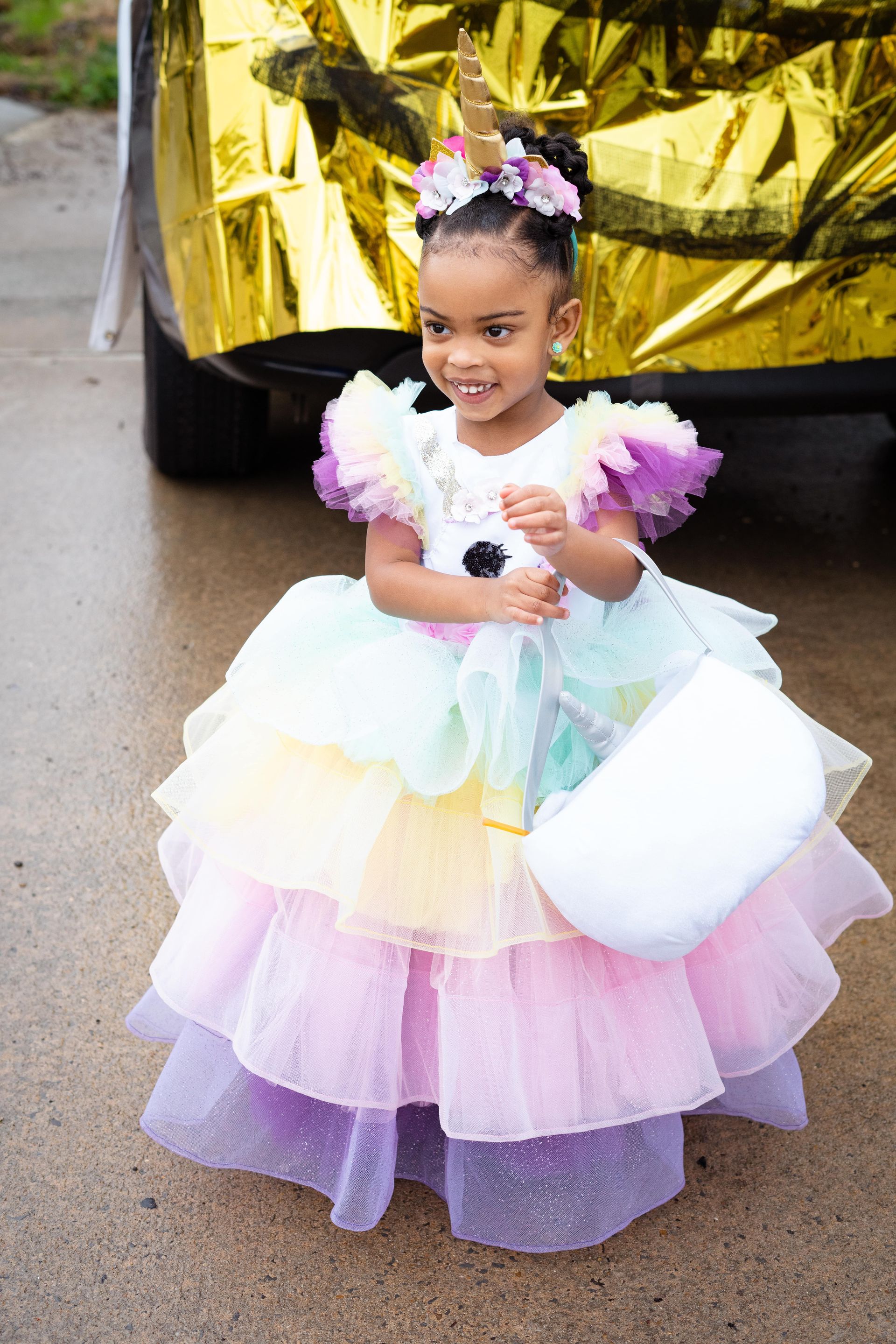 A little girl in a unicorn costume is standing in front of a car.