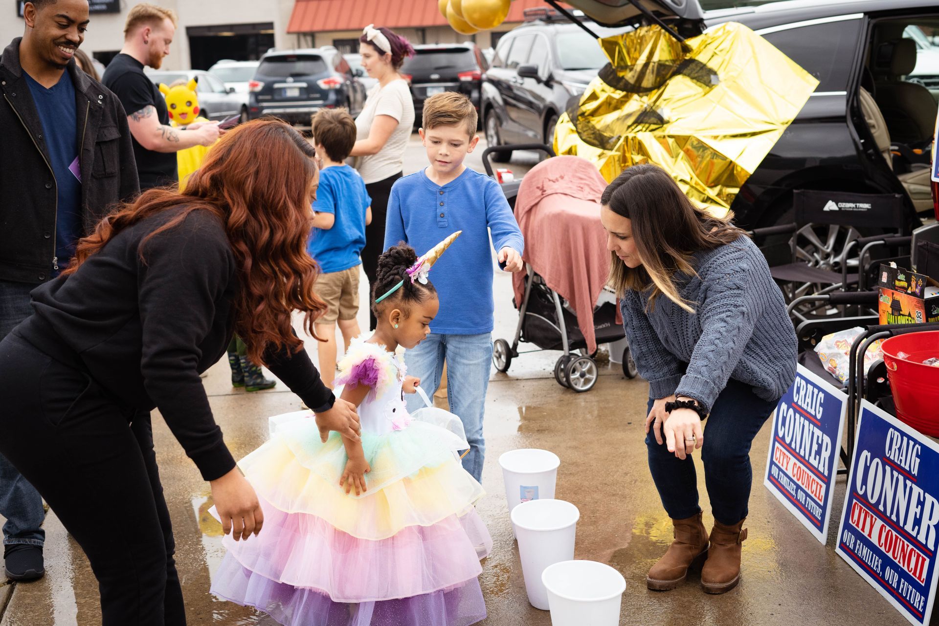 A group of people are standing around a little girl in a unicorn dress.