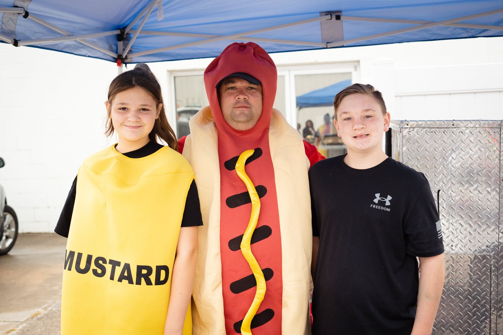 A man in a hot dog costume is standing next to two children.