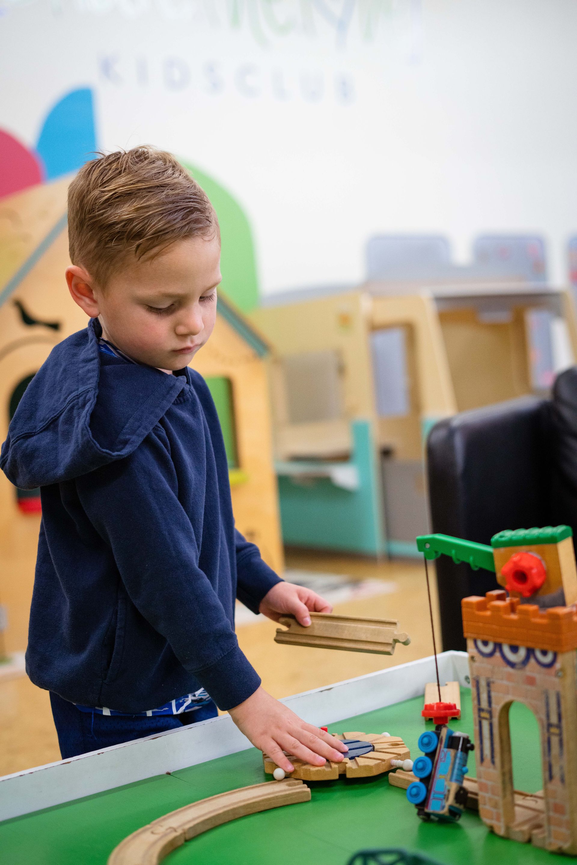 A young boy is playing with a wooden train set on a table.