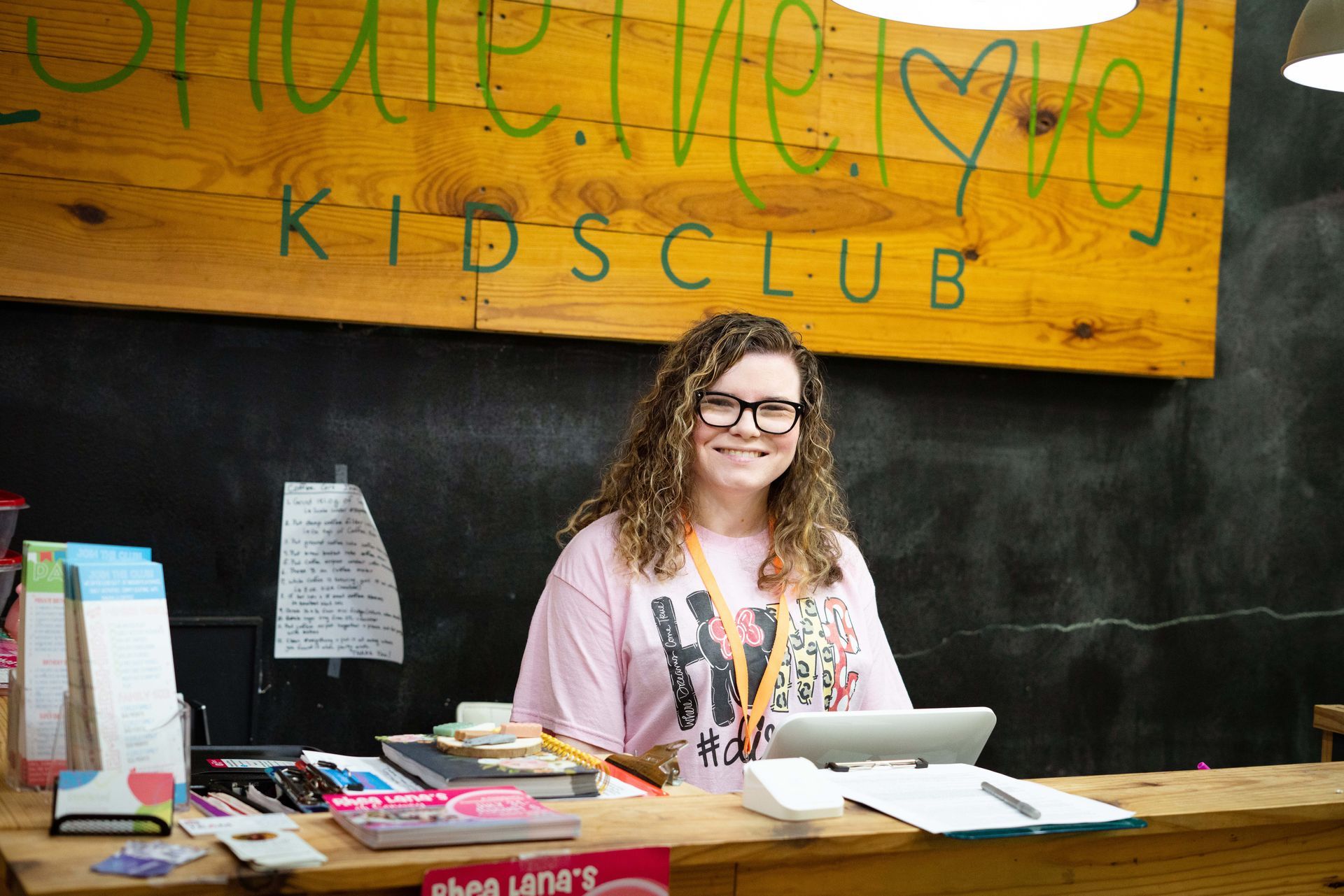 A woman is sitting at a desk in front of a sign that says kids club.