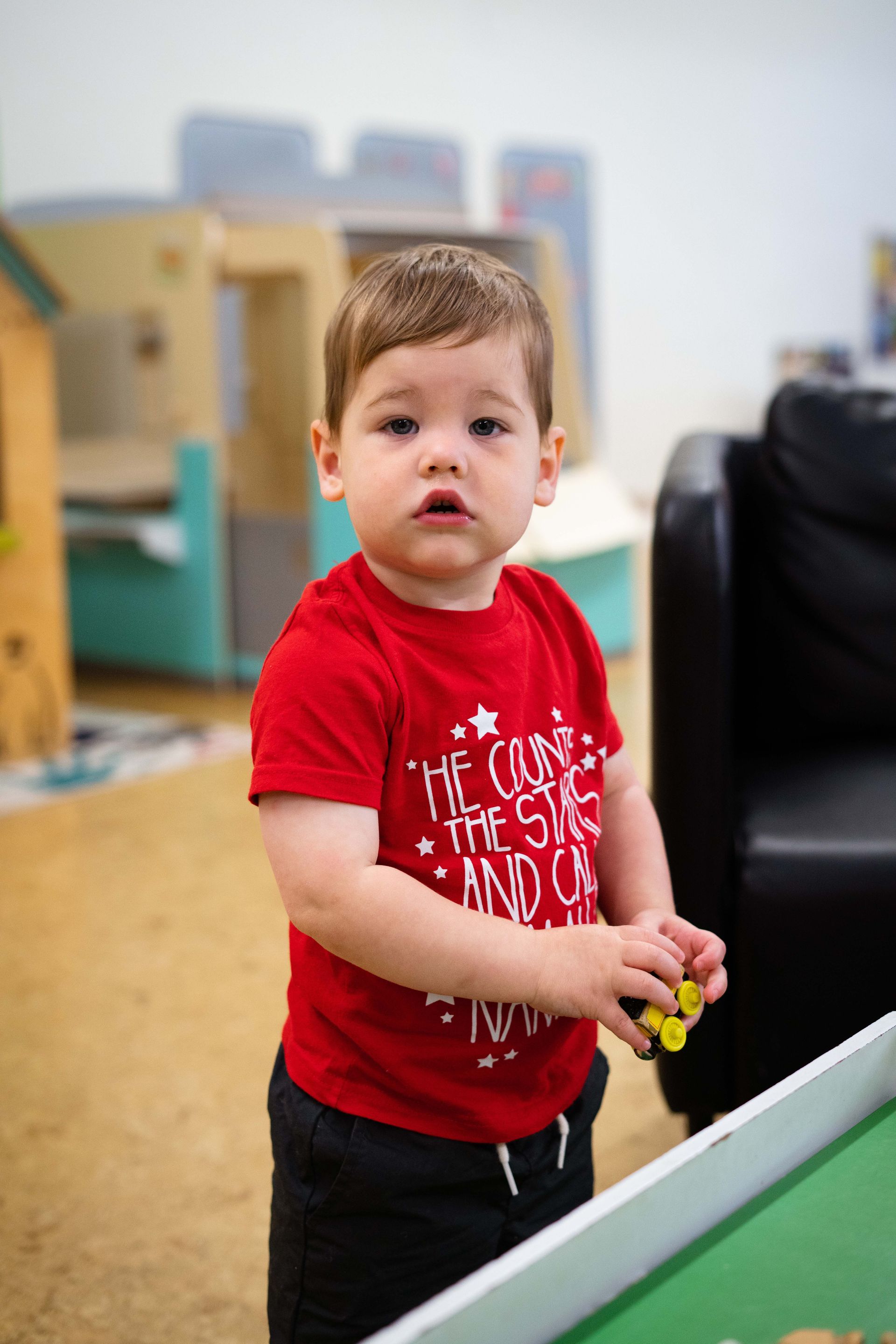 A little boy in a red shirt is standing next to a table.