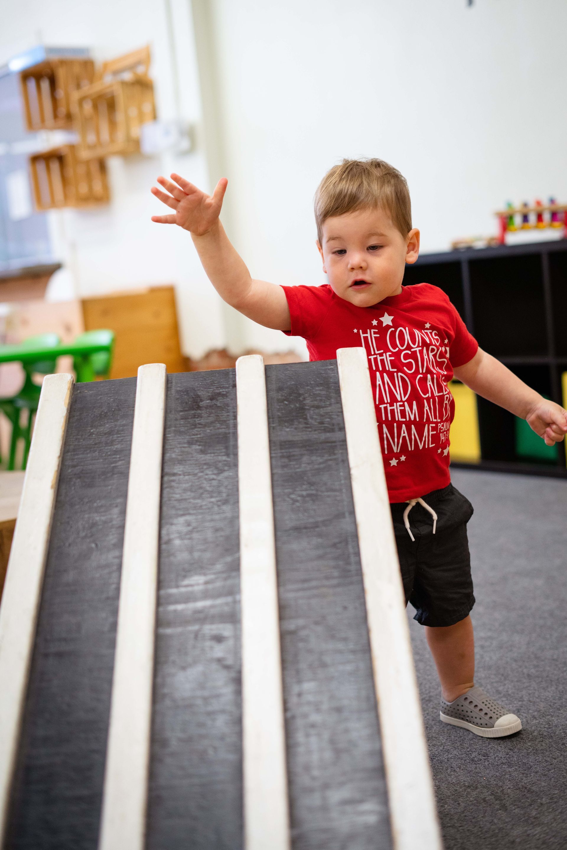 A young boy is playing with a wooden ramp in a classroom.