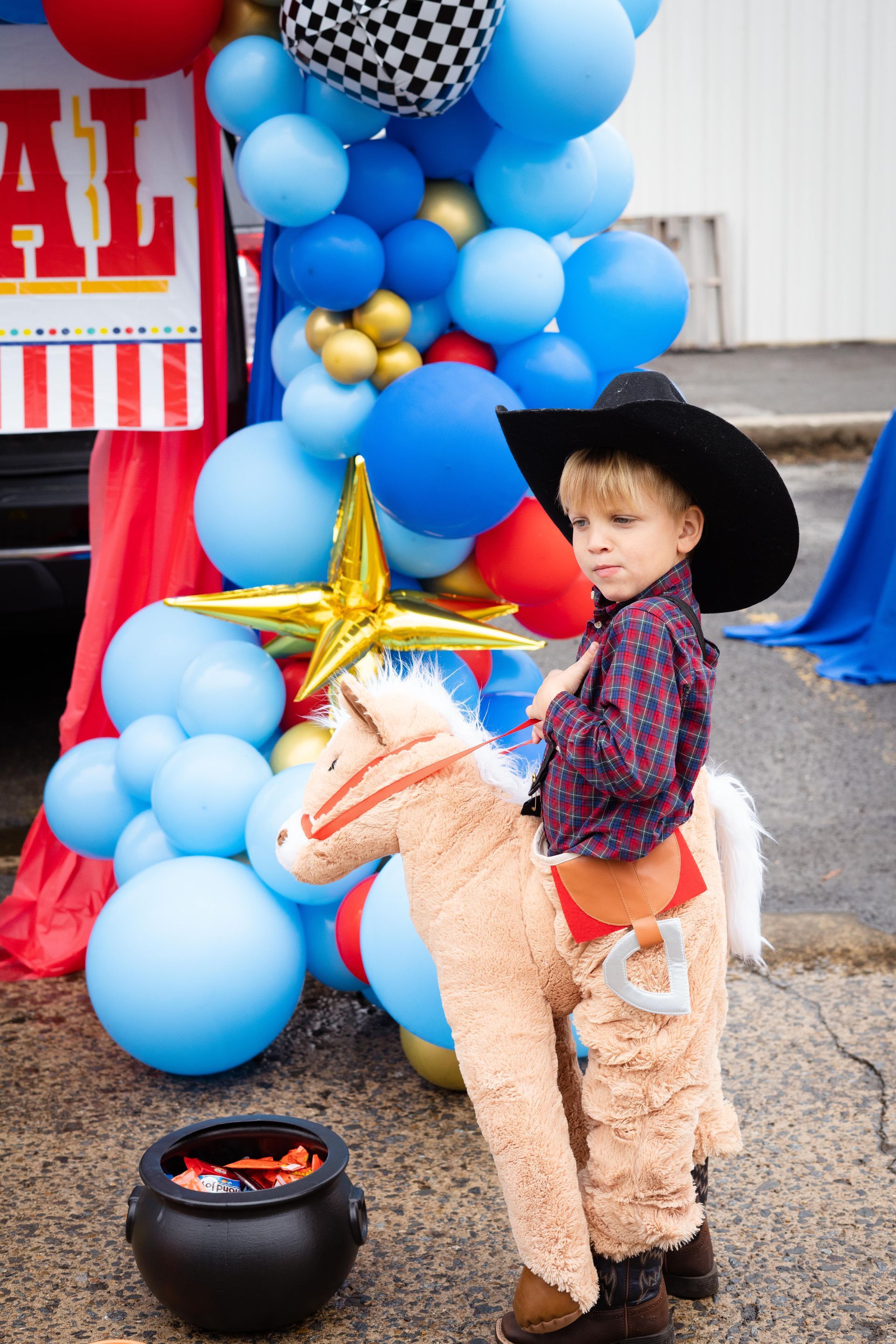 A little boy in a cowboy costume is standing next to a stuffed horse.