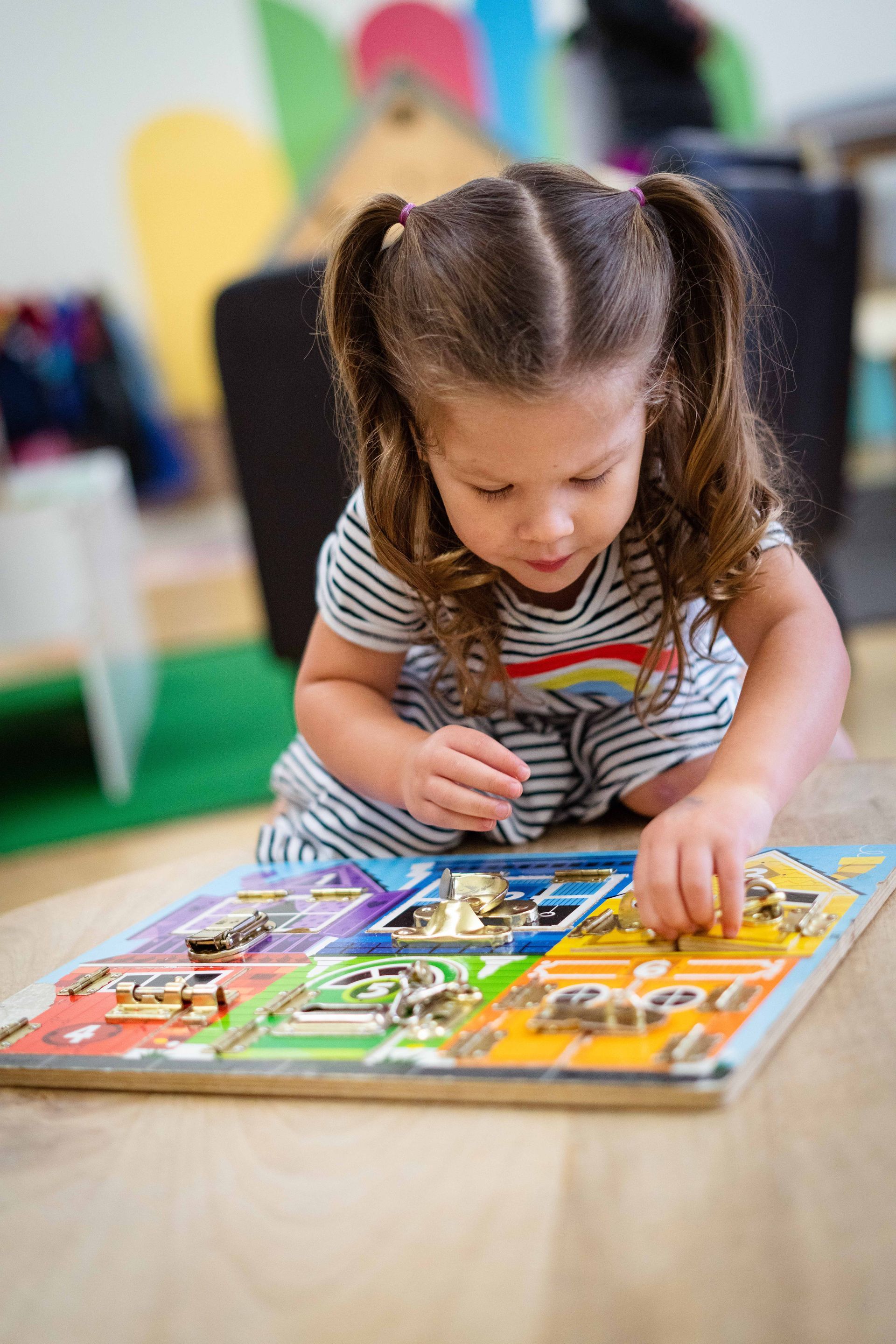 A little girl is playing with a wooden puzzle on the floor.