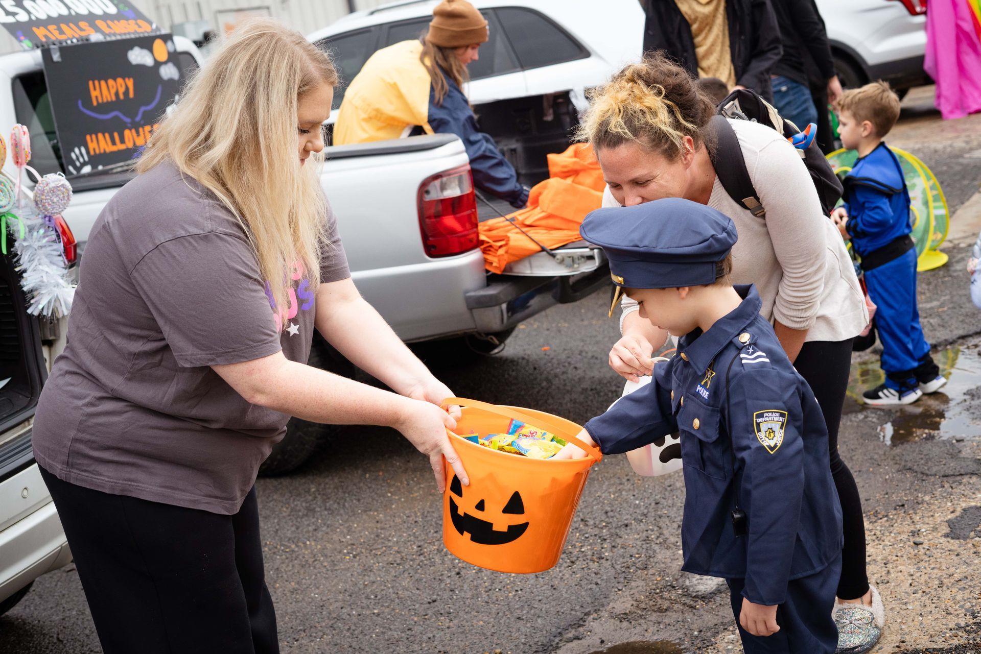 A woman in a police uniform is handing a child a bucket of candy.