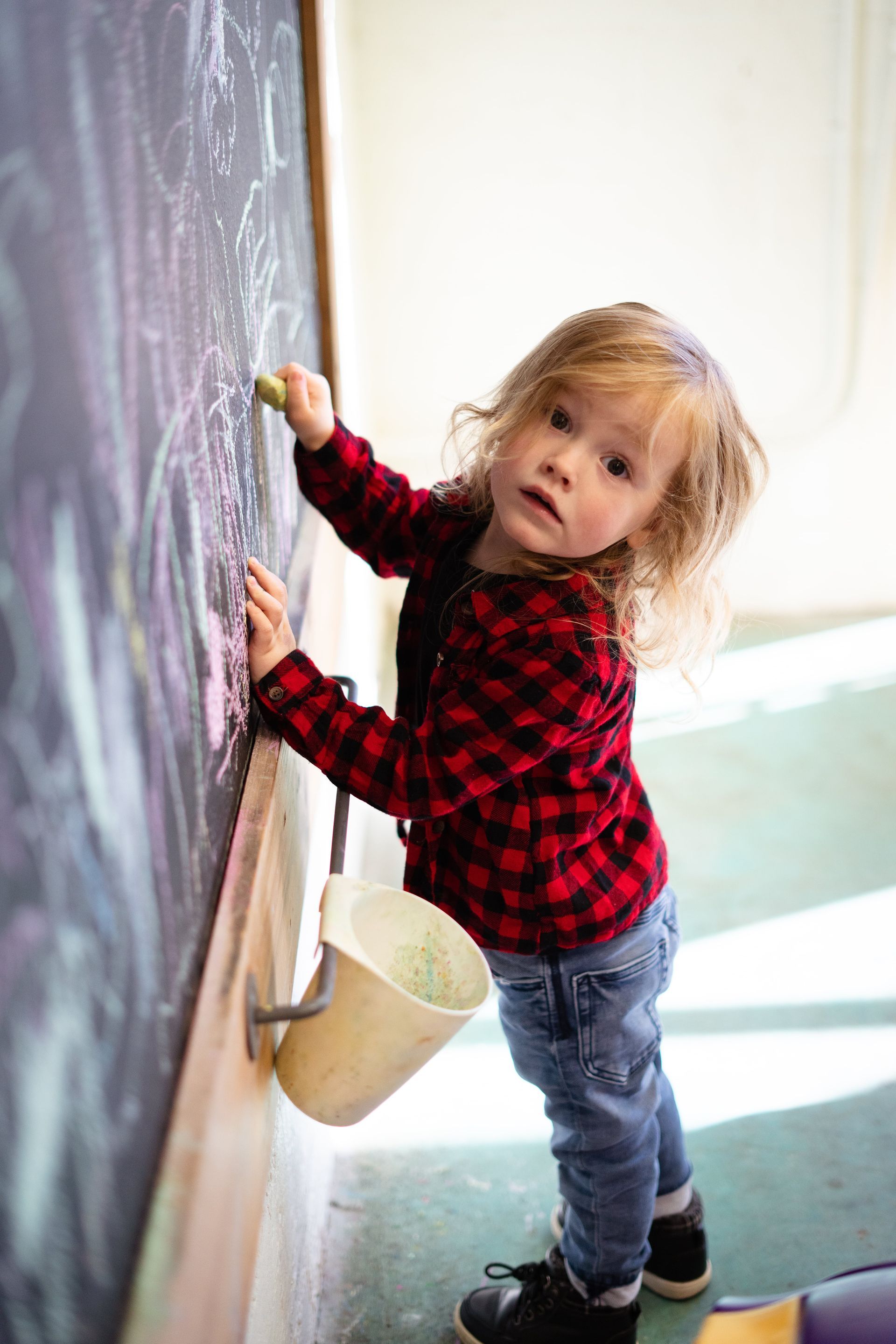 A little girl is writing on a blackboard with chalk.