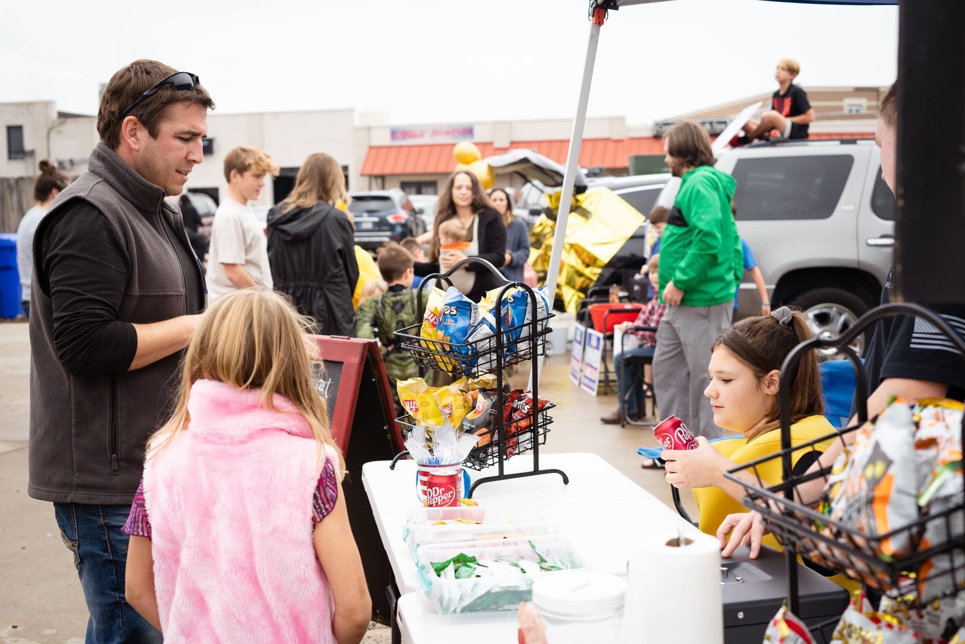 A group of people are standing around a table in a parking lot.