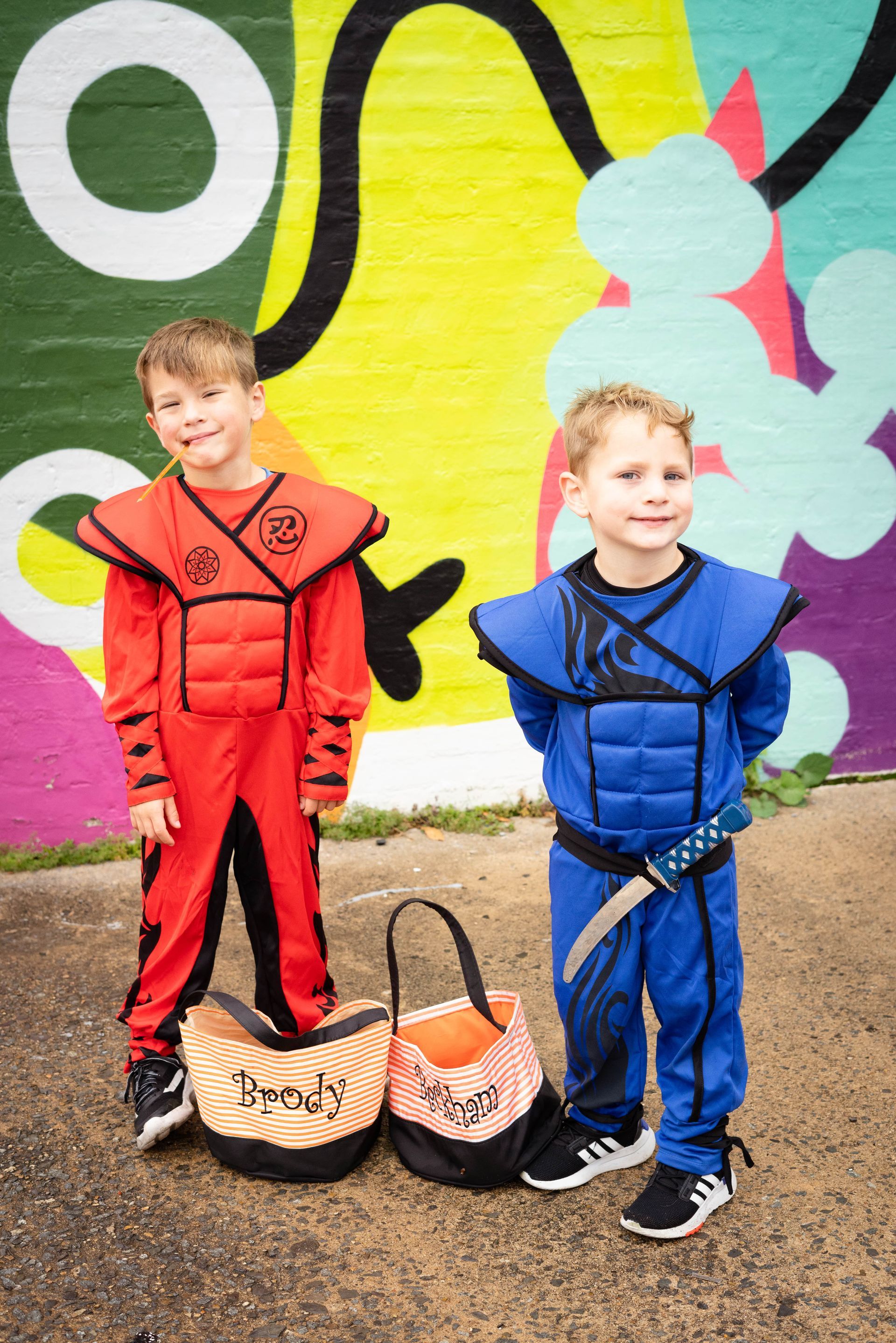 Two young boys in halloween costumes are standing next to each other in front of a graffiti wall.