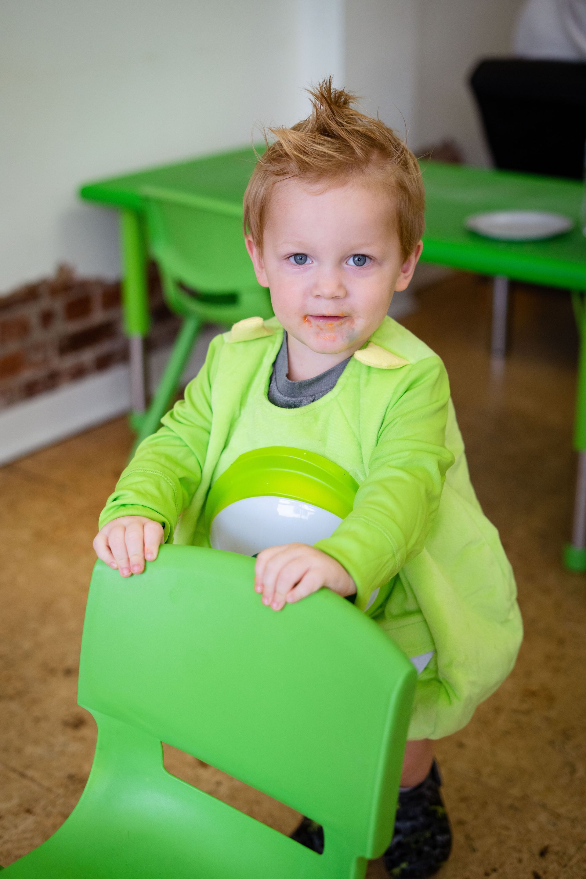 A little boy in a shrek costume is sitting on a green chair.