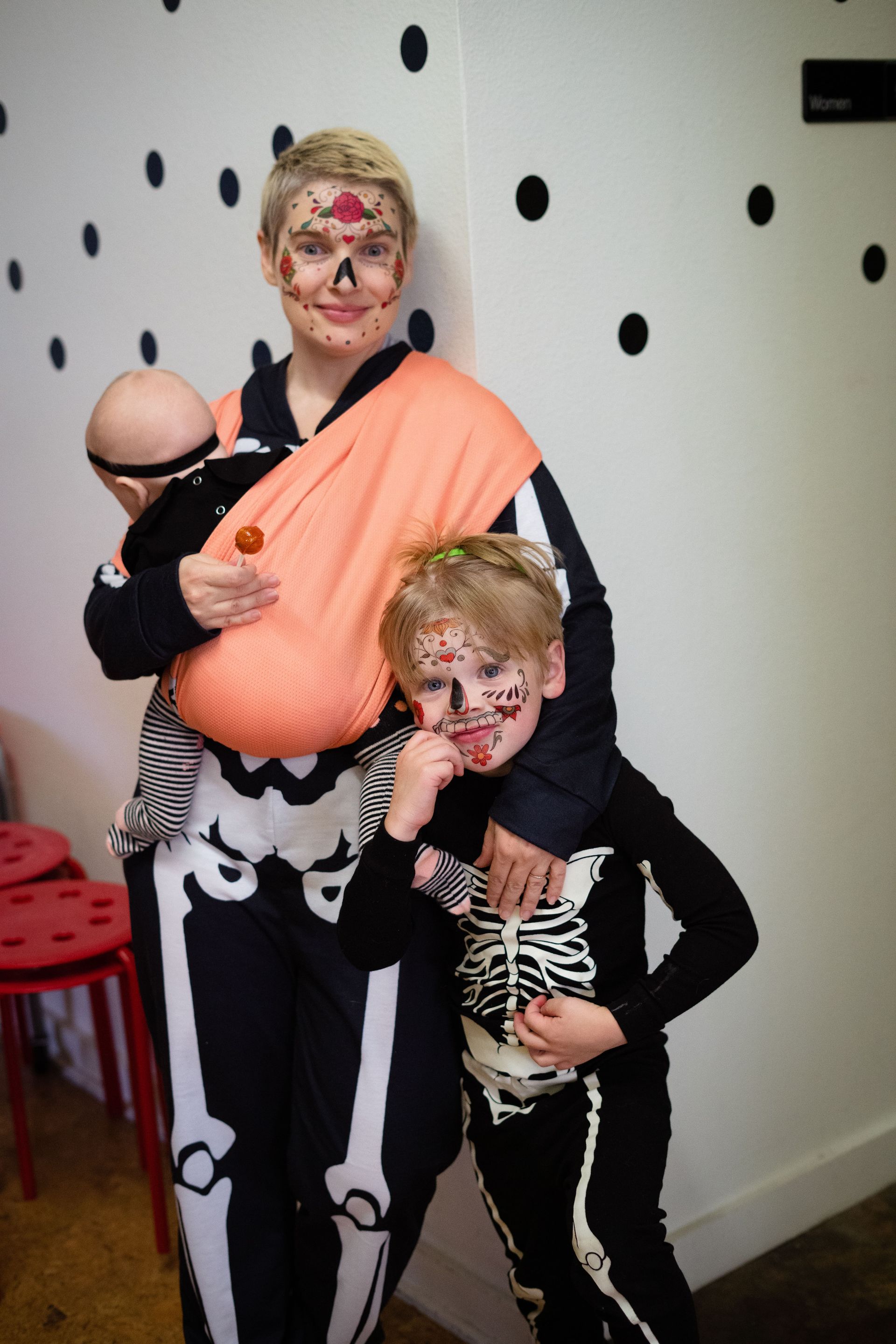 A woman in a skeleton costume is holding a baby and two children