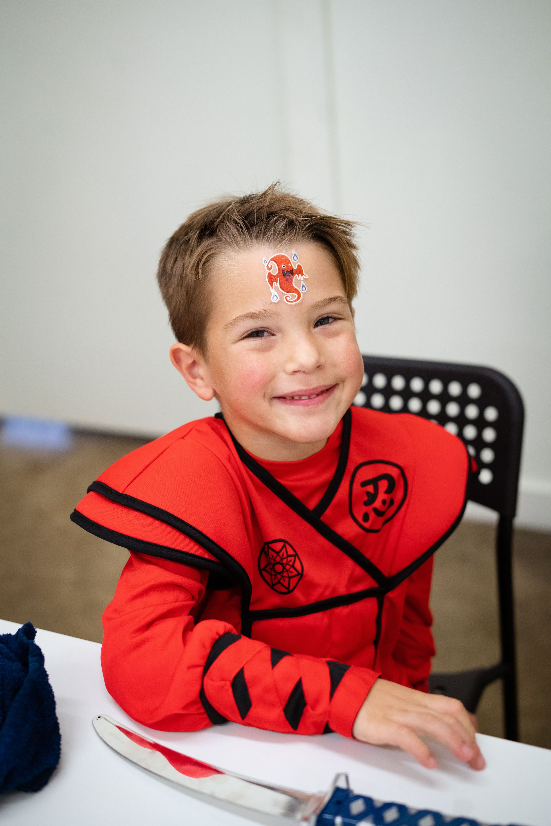 A young boy in a red ninja costume is sitting at a table.