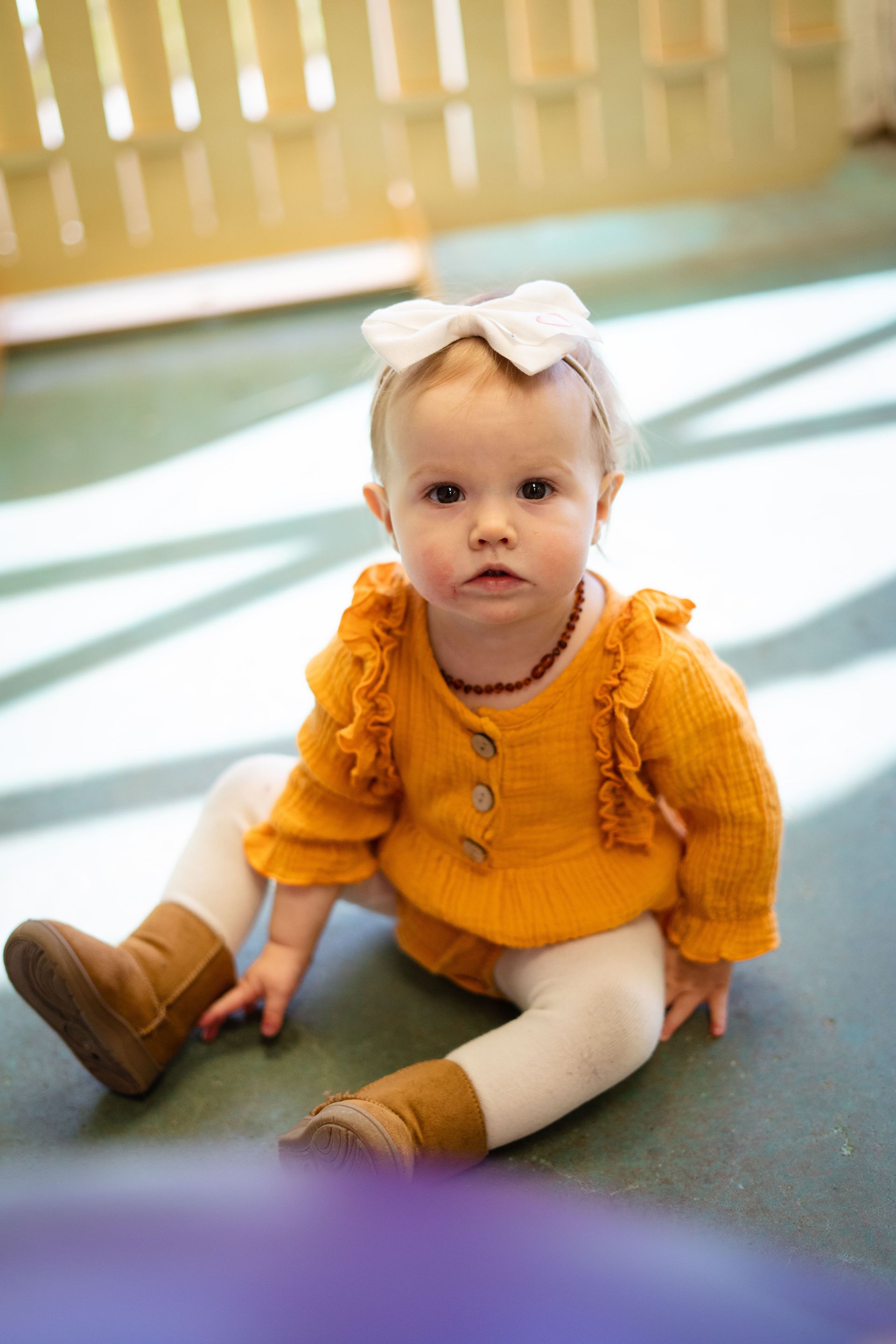 A baby girl is sitting on the floor wearing a yellow sweater and white tights.