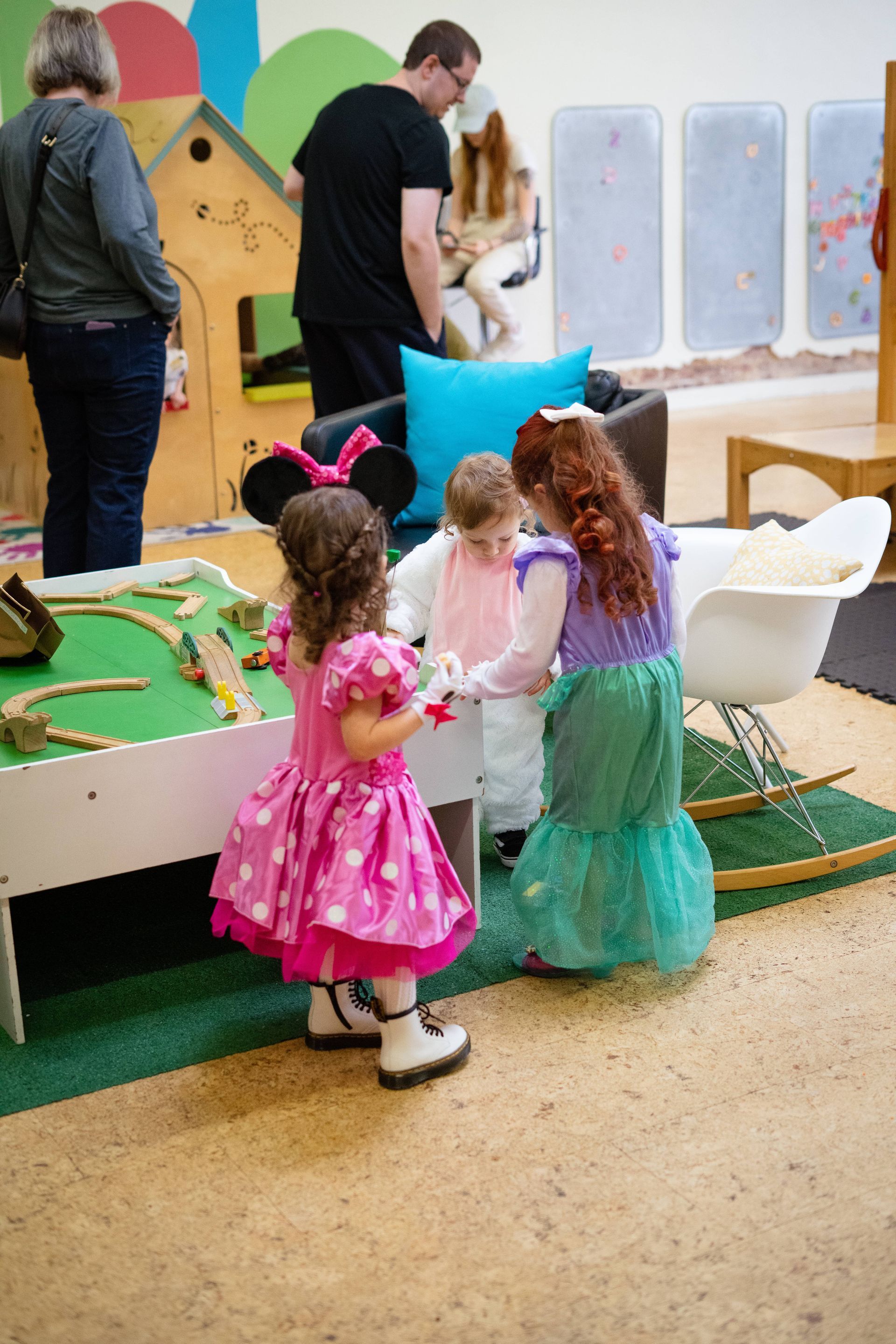 Three little girls in dresses are standing next to each other in a room.