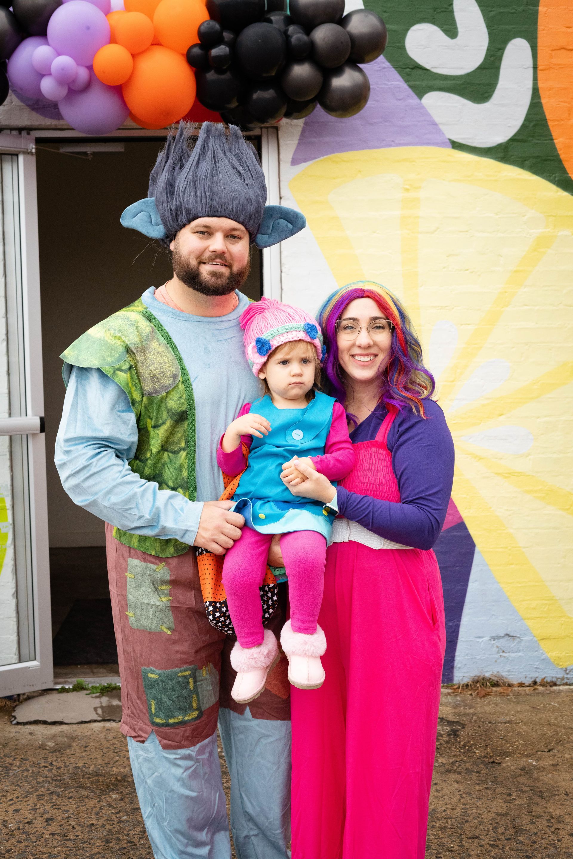 A man , woman , and child are dressed in troll costumes and posing for a picture.