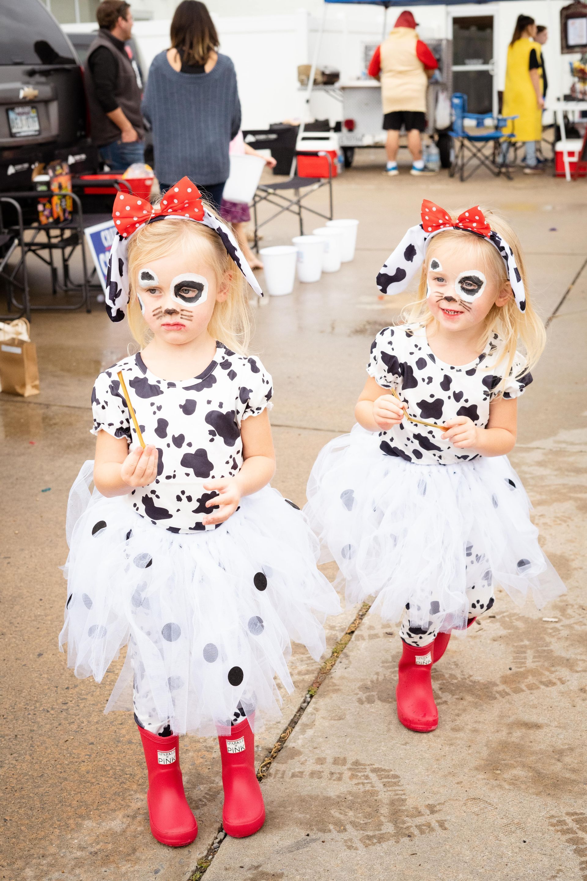 Two little girls in dalmatian costumes are standing next to each other on a sidewalk.