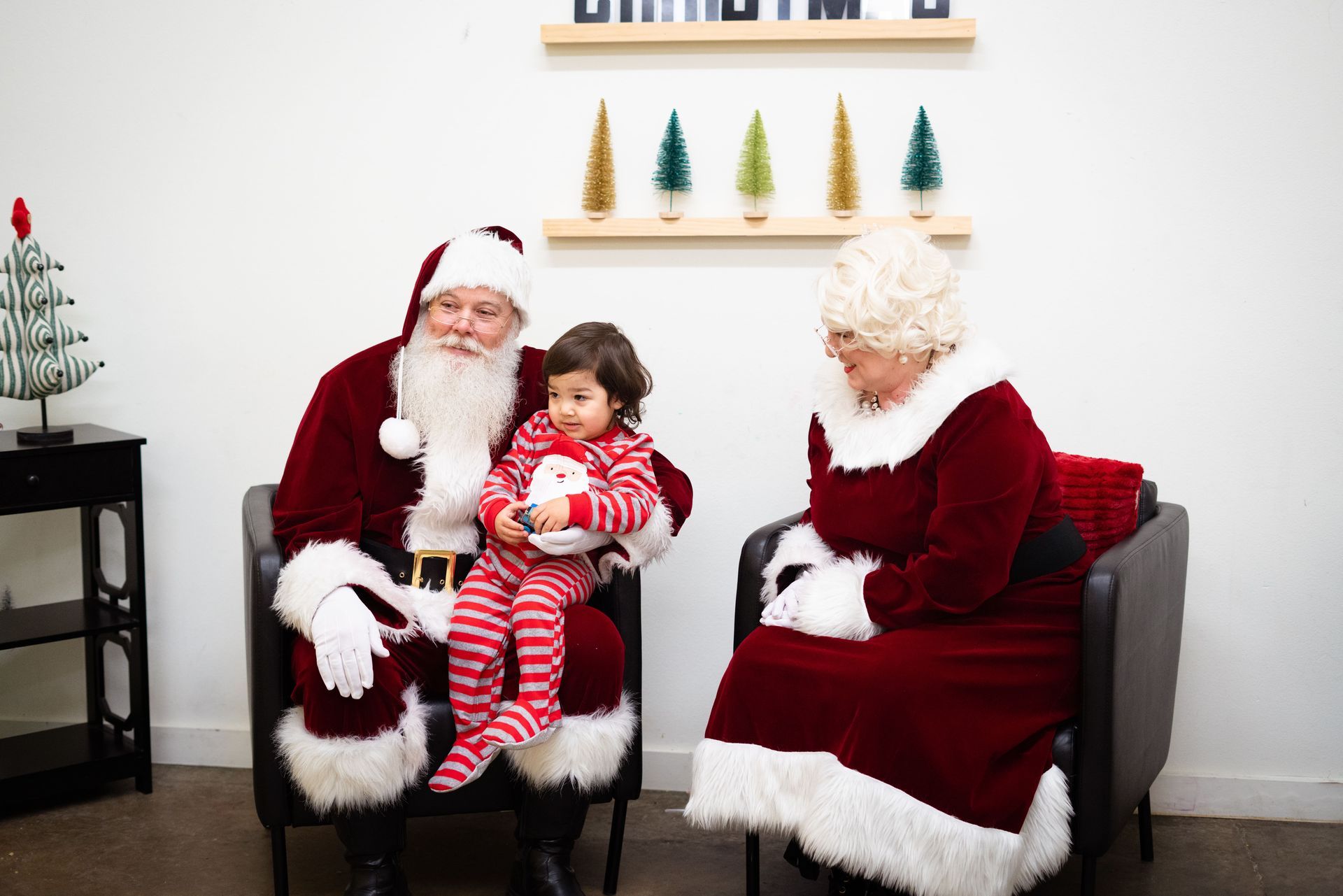 Santa claus and mrs. claus are sitting in chairs holding a little girl.