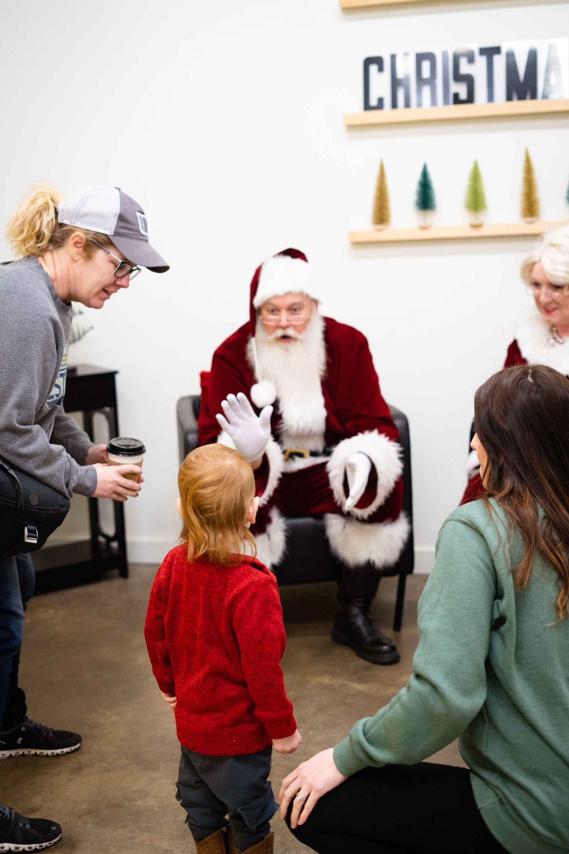 A little girl is standing in front of santa claus in a room.