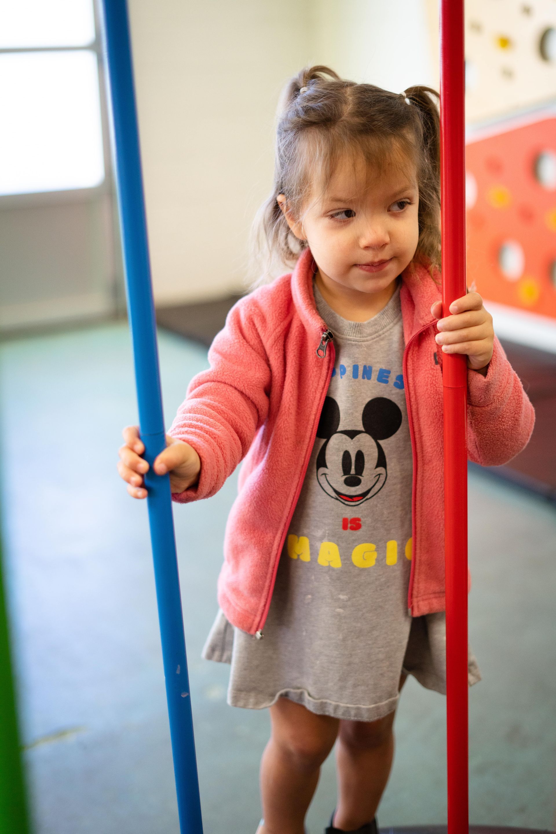 A little girl in a mickey mouse shirt is holding a red and blue pole.