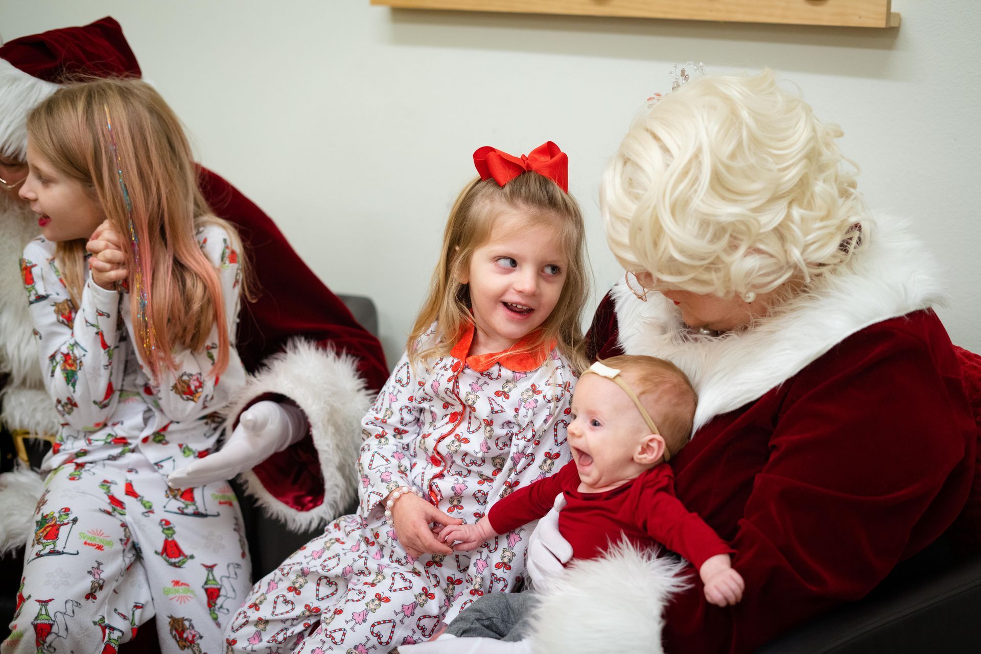 A baby is sitting on the lap of a woman dressed as santa claus.