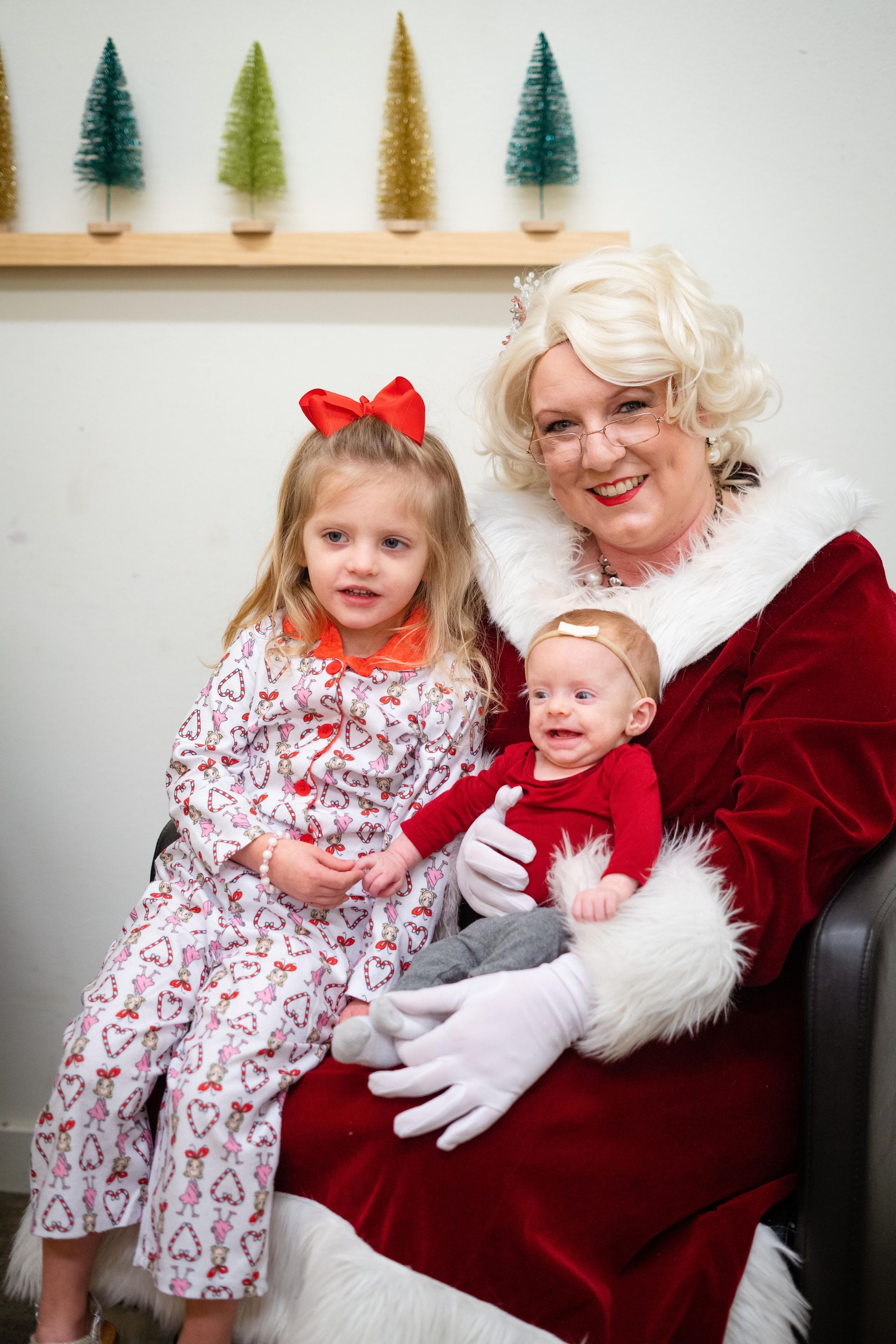 A woman dressed as santa claus is holding a baby and two little girls.
