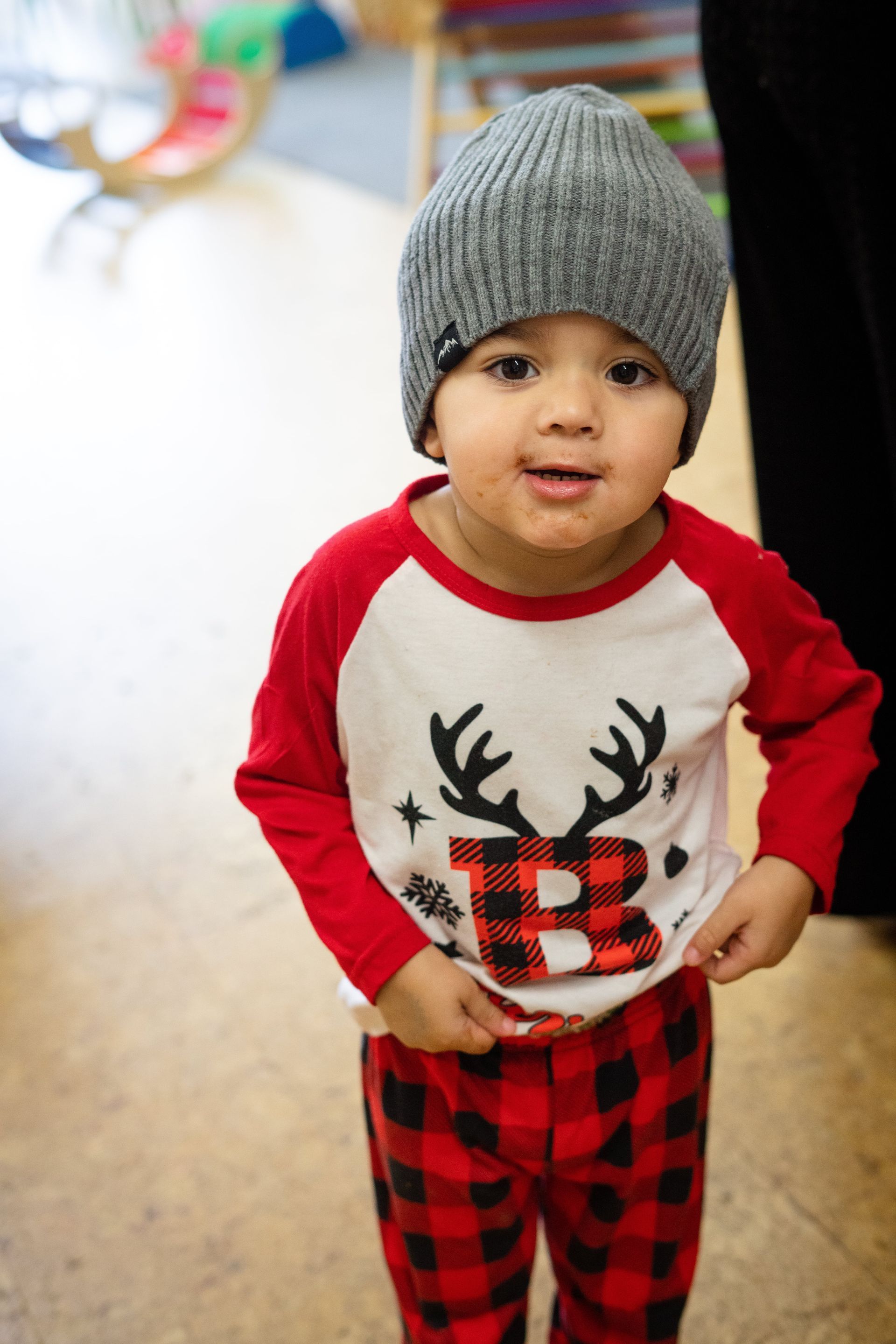 A little boy wearing a hat and a plaid shirt with a reindeer on it