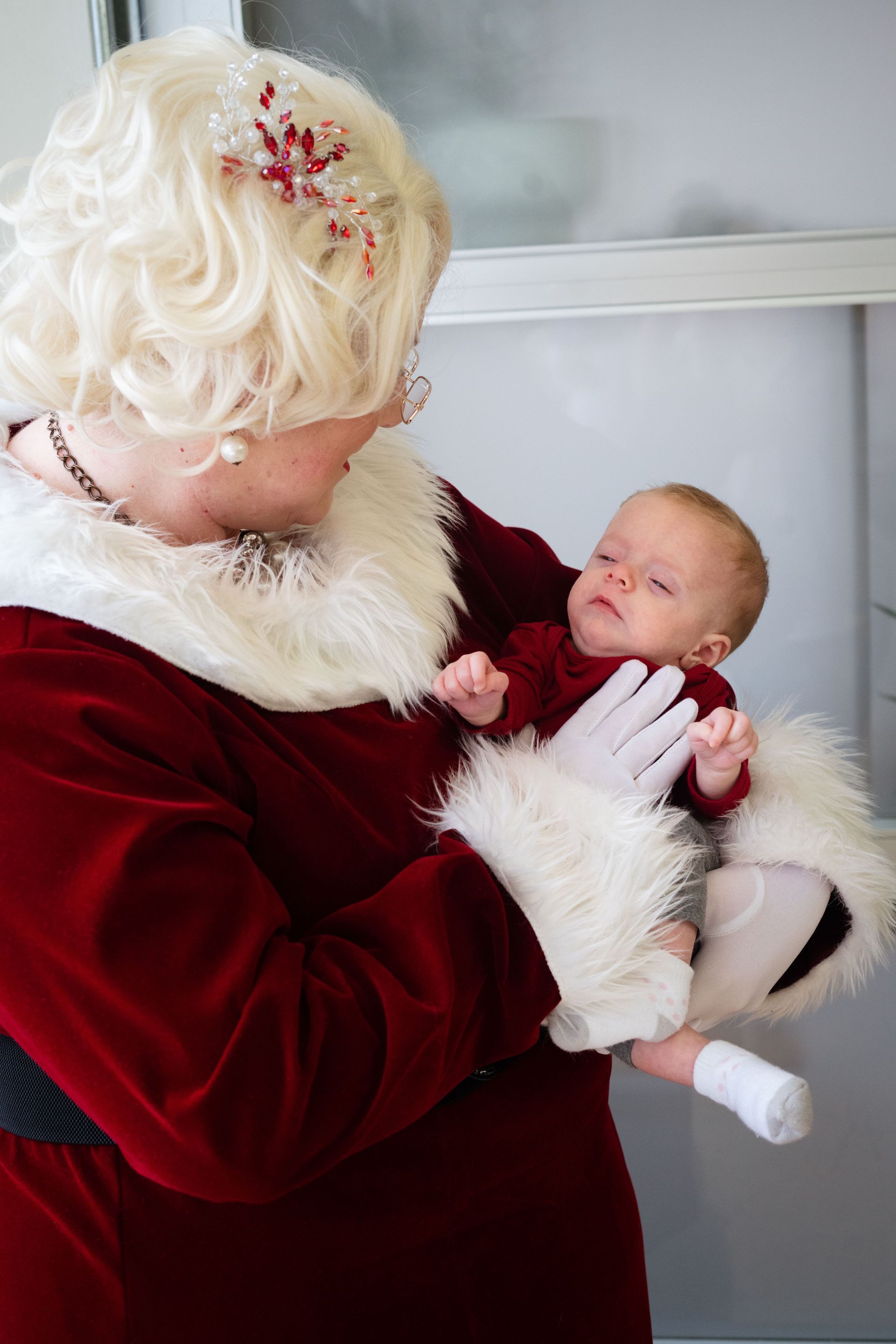 A woman dressed as santa claus is holding a baby in her arms.