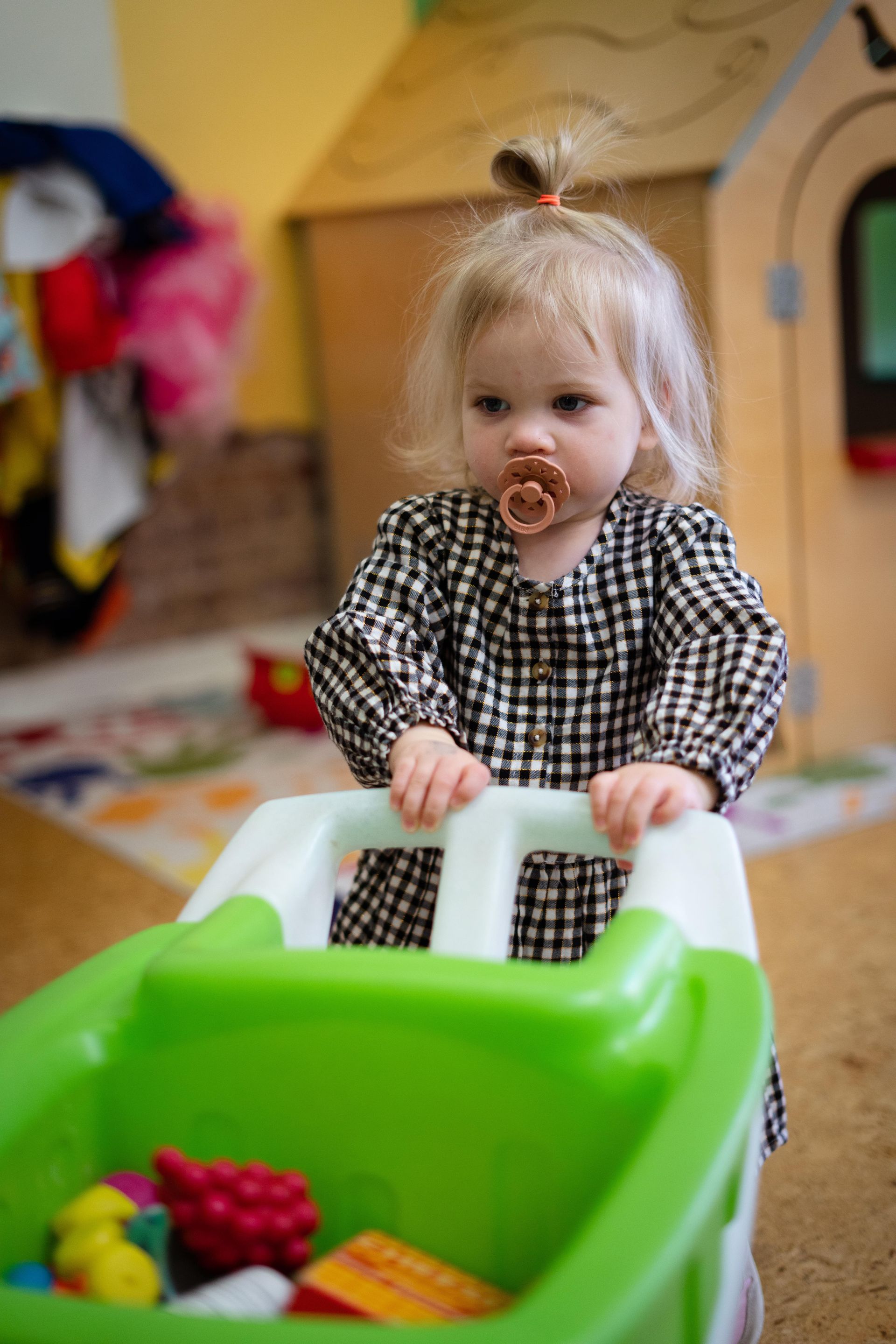 A little girl is sitting in a high chair with a pacifier in her mouth.