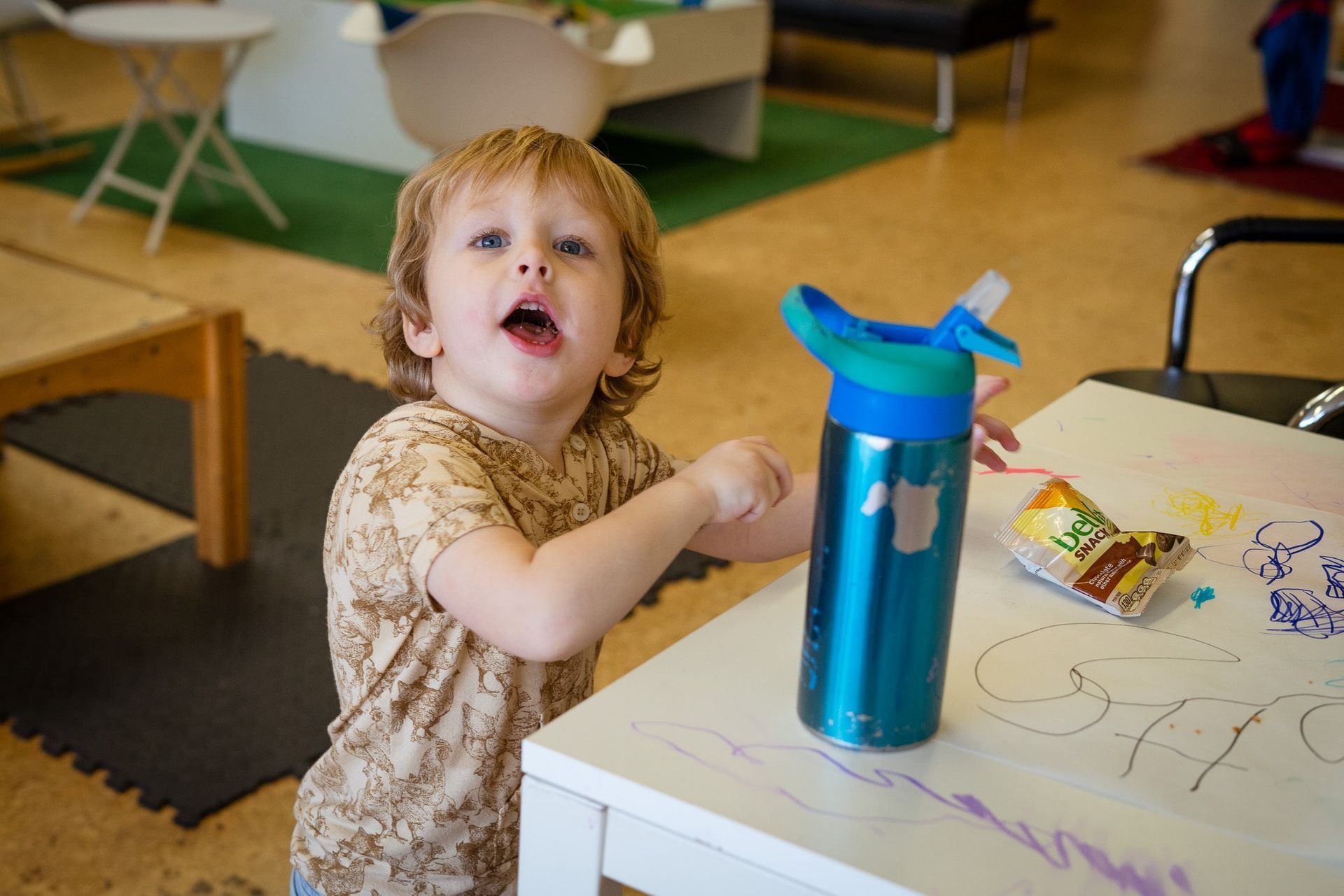 A little boy is standing at a table with a water bottle.