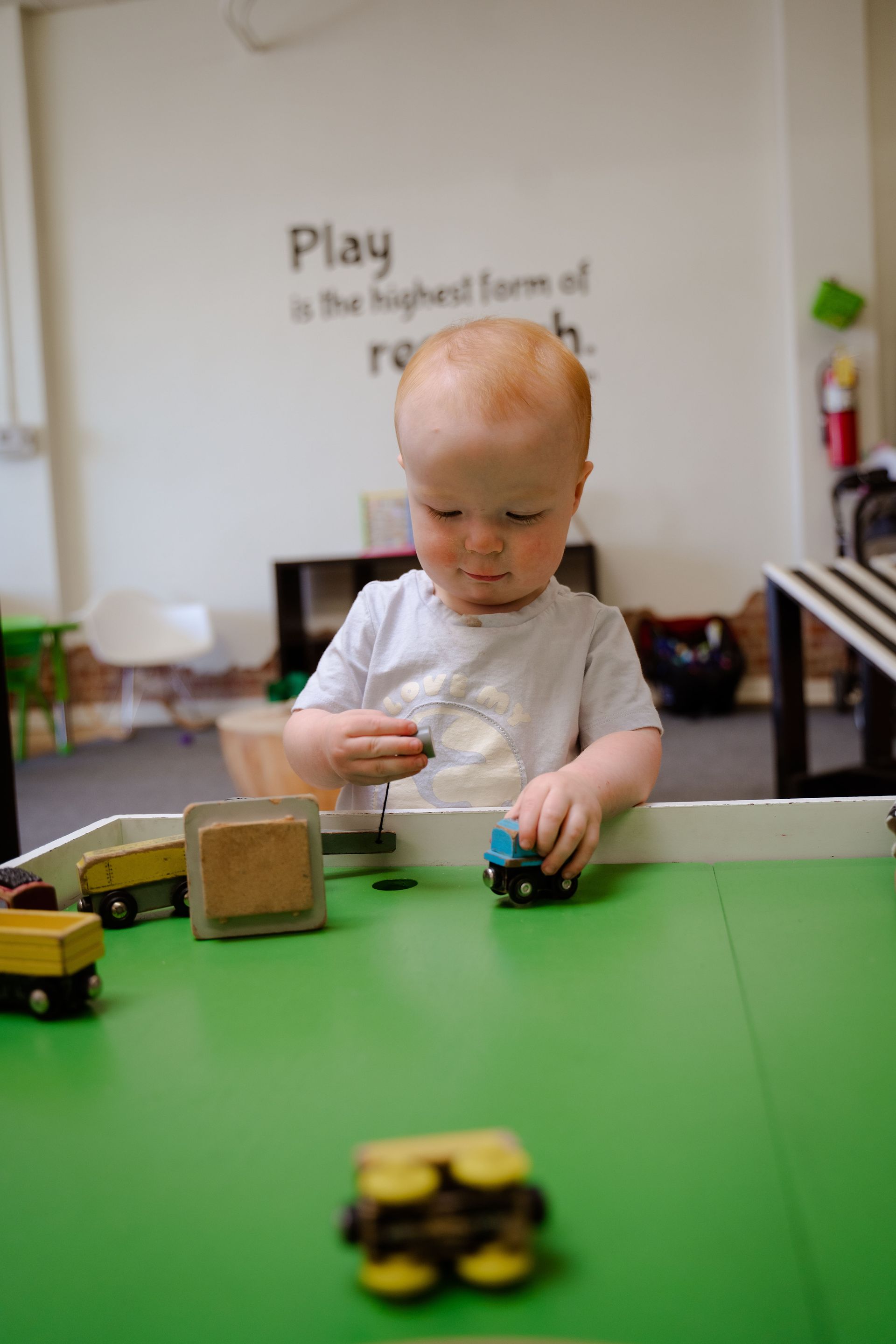 A baby is playing with a toy train on a green table.