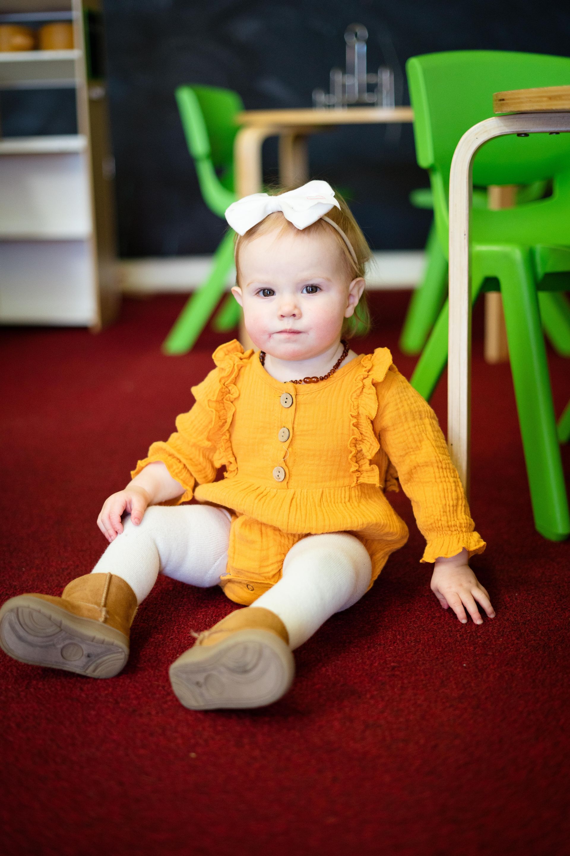 A little girl is sitting on the floor in a room with green chairs.