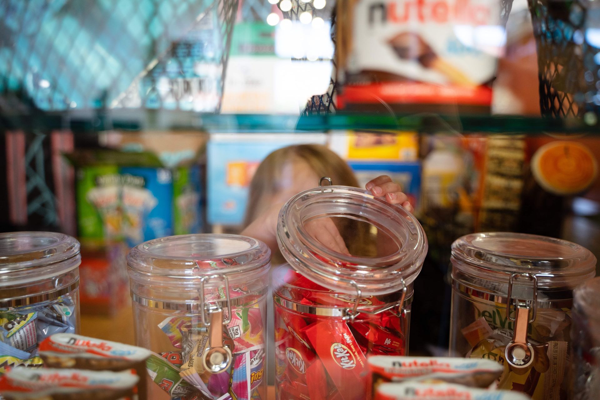 A little girl is looking into a jar of candy.