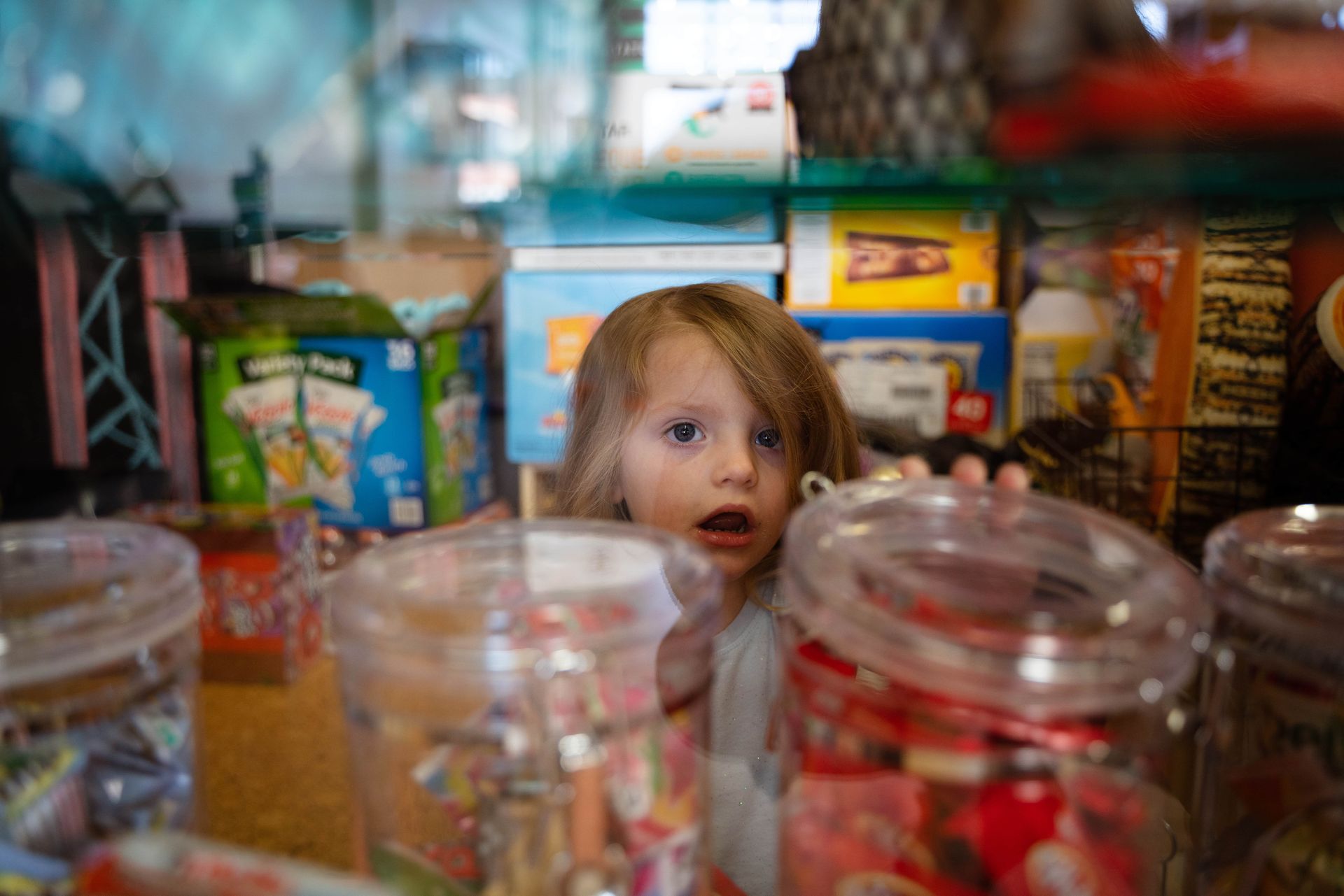 A little girl is looking at jars of candy in a store.
