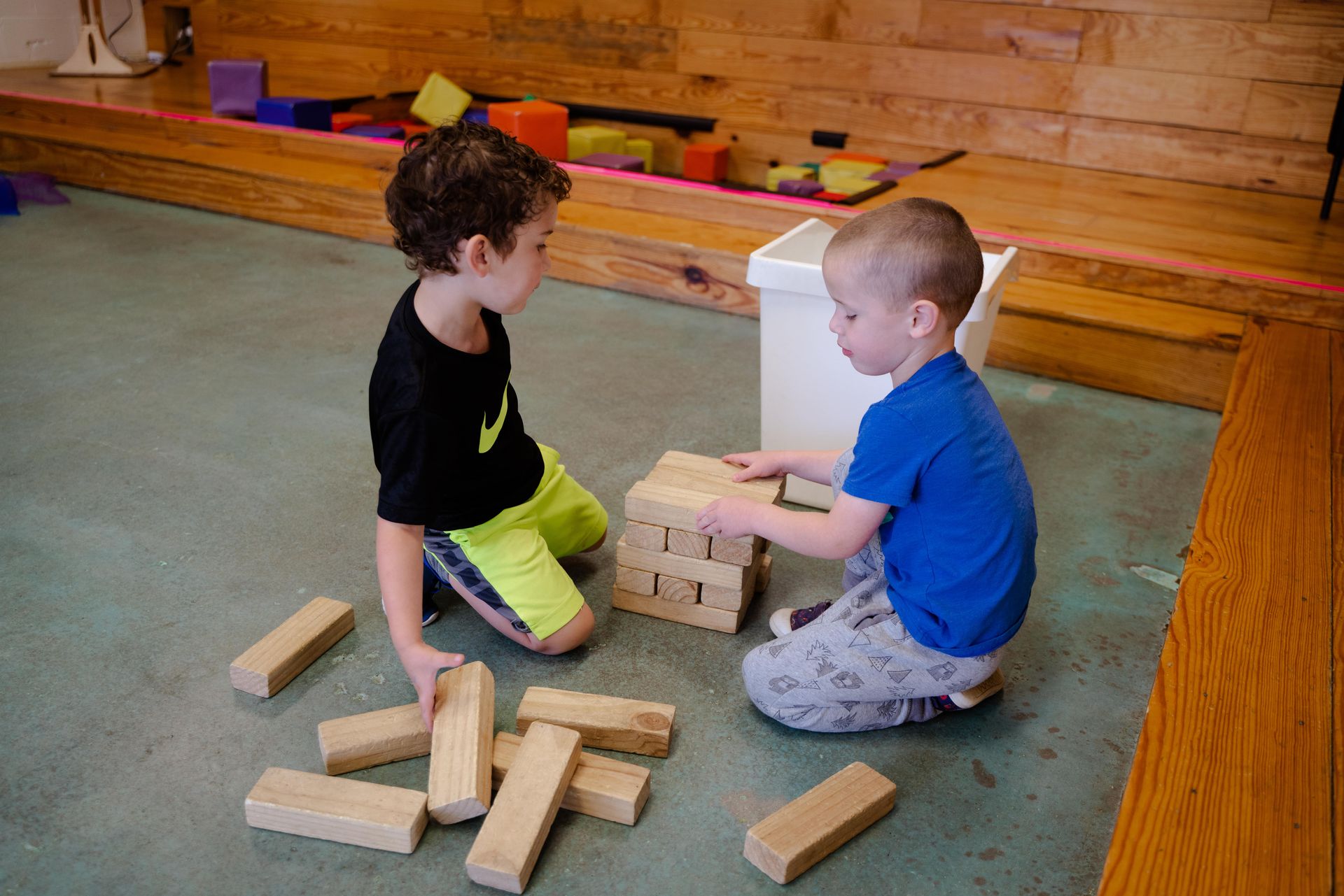 Two young boys are playing with wooden blocks on the floor.