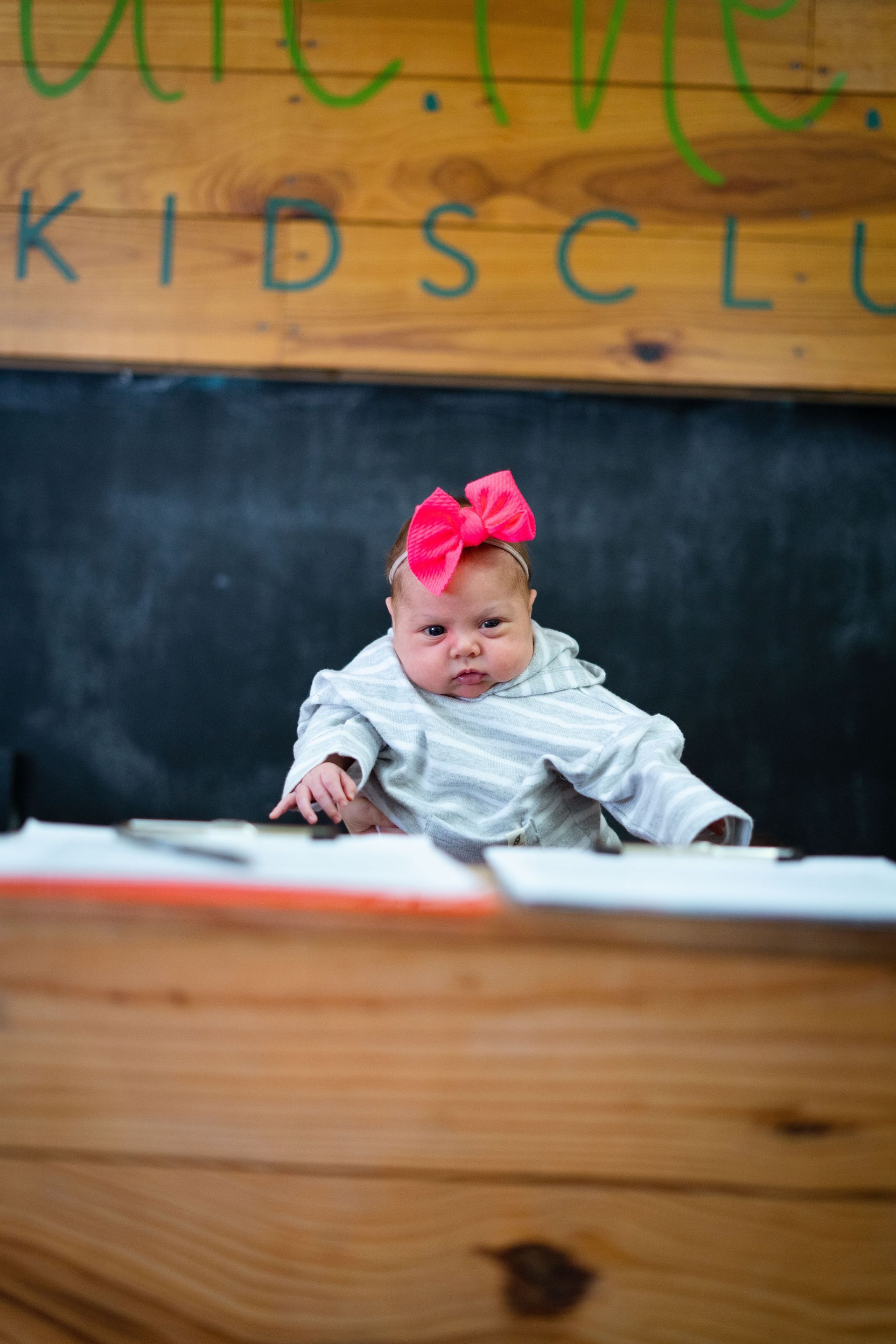 A baby with a red bow on her head is sitting at a desk