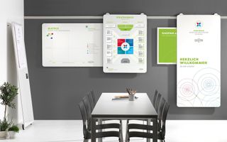 Meeting room with whiteboard, displays, table, chairs, and plants against a gray wall.