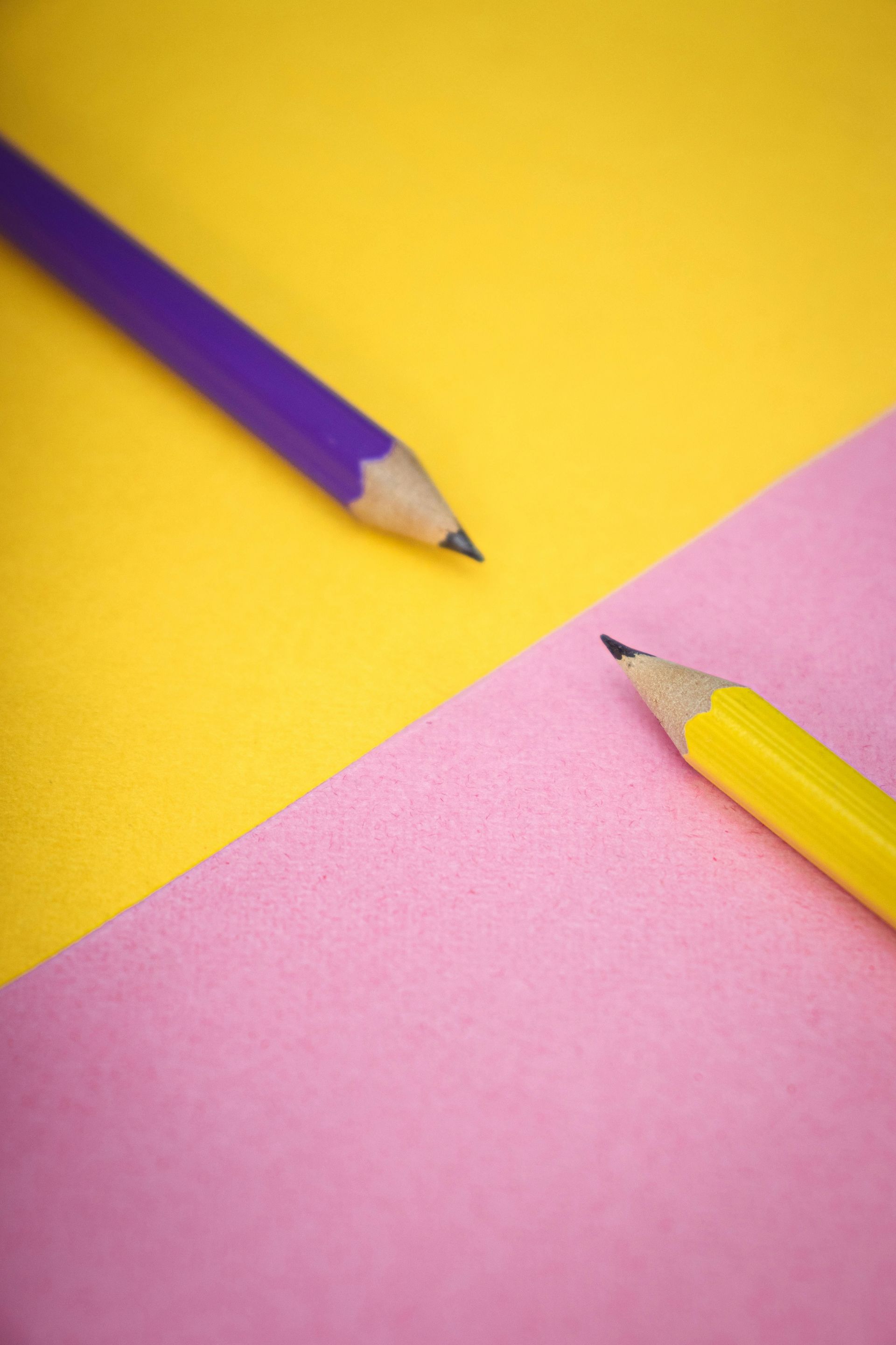 Purple and yellow pencils on yellow and pink diagonal backgrounds.
