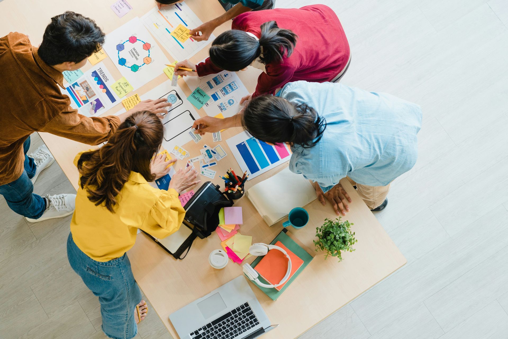 People brainstorming around a table, working on papers, with colors and items.