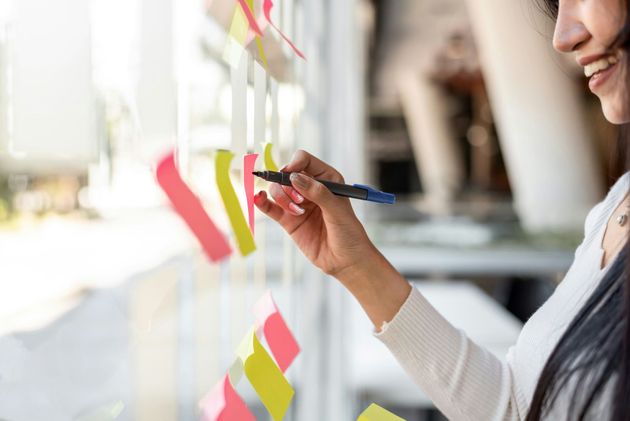 Woman writes on sticky note on window with bright sunlight.