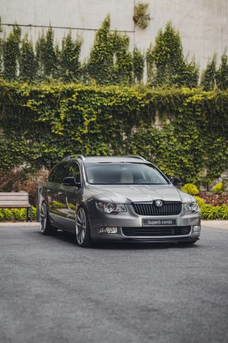 Gray Skoda Superb sedan parked, set against a wall covered in green ivy.