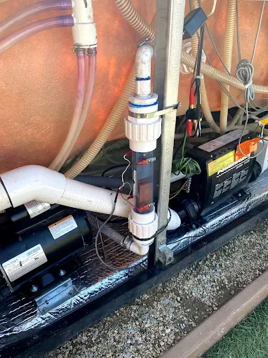 Pool pump and filtration plumbing with black equipment mounted on a wet concrete pad.
