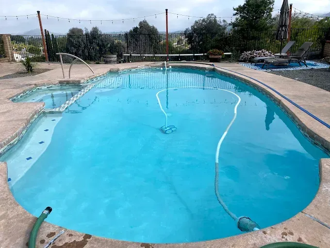 Empty turquoise swimming pool with a curved edge and deck chairs in the background